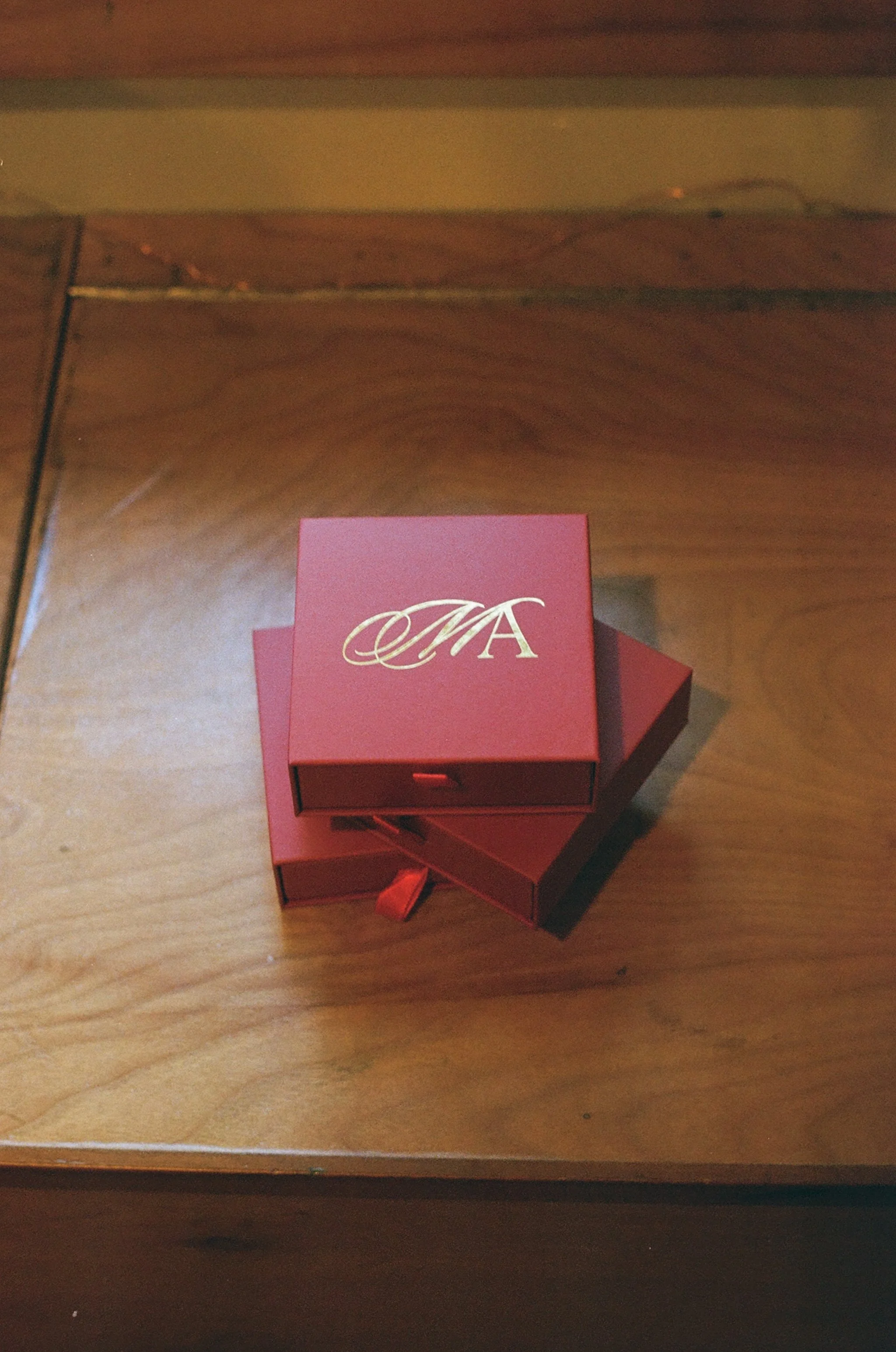 Red gift box with a gold monogram ribbon on a wooden table