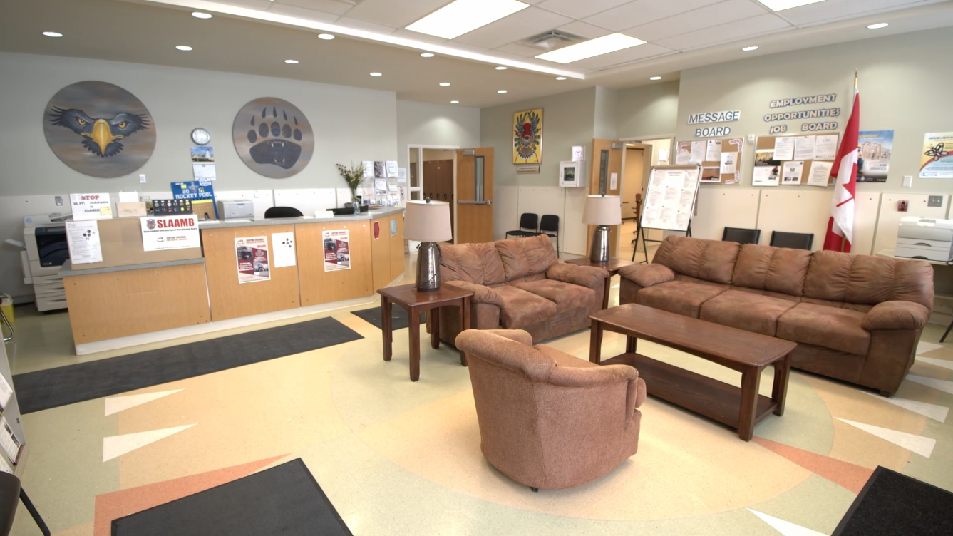 Welcoming community center lobby with reception desk, couches, bulletin boards, and Canadian flag