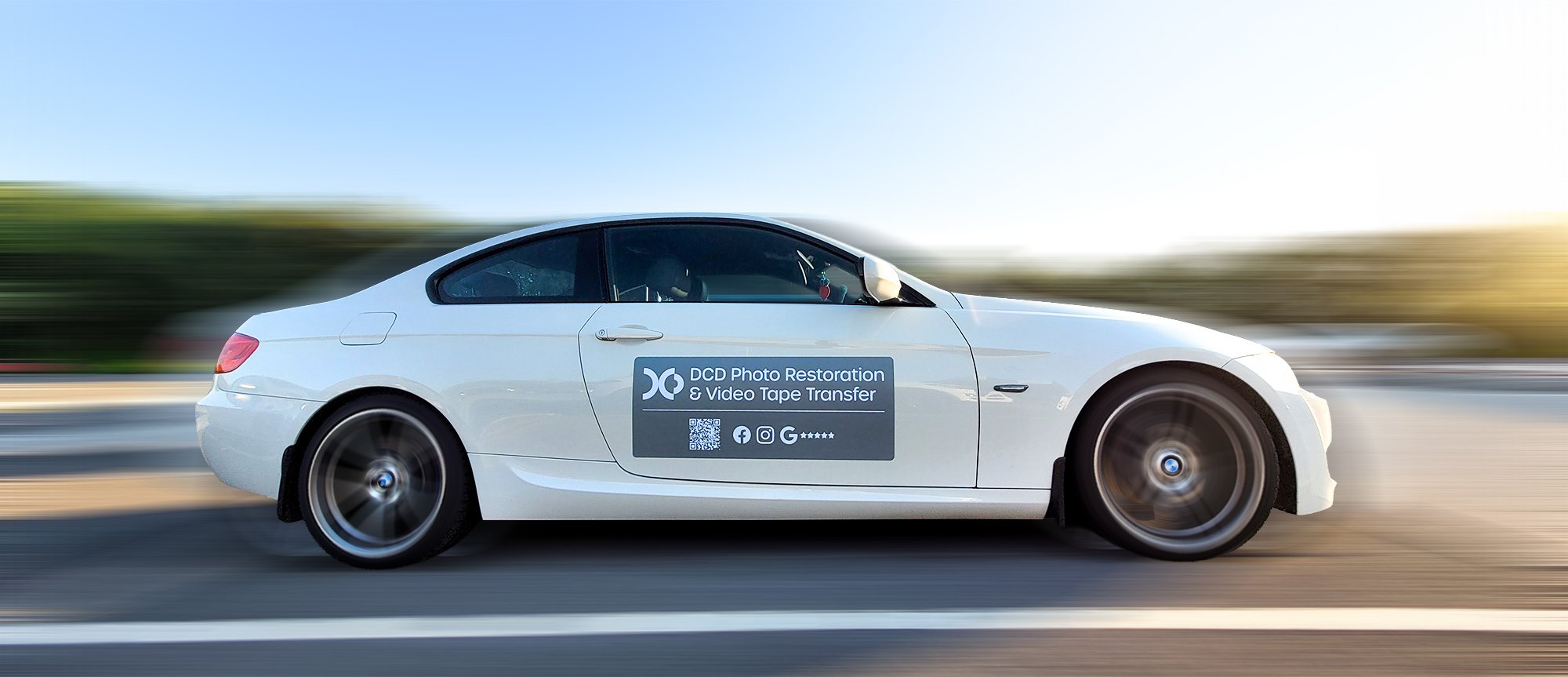 White sports car in motion on a road with blurred background, advertising DCD Photo Restoration & Video Tape Transfer on the side door.