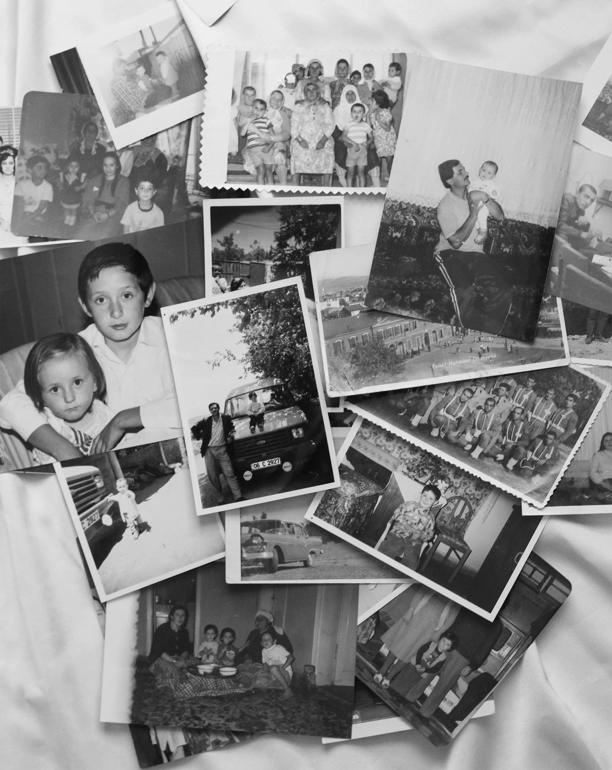 A collection of black-and-white photographs spread out on a surface, featuring people of different ages, some smiling, some in candid moments, with scenes including children, adults, and outdoor settings.