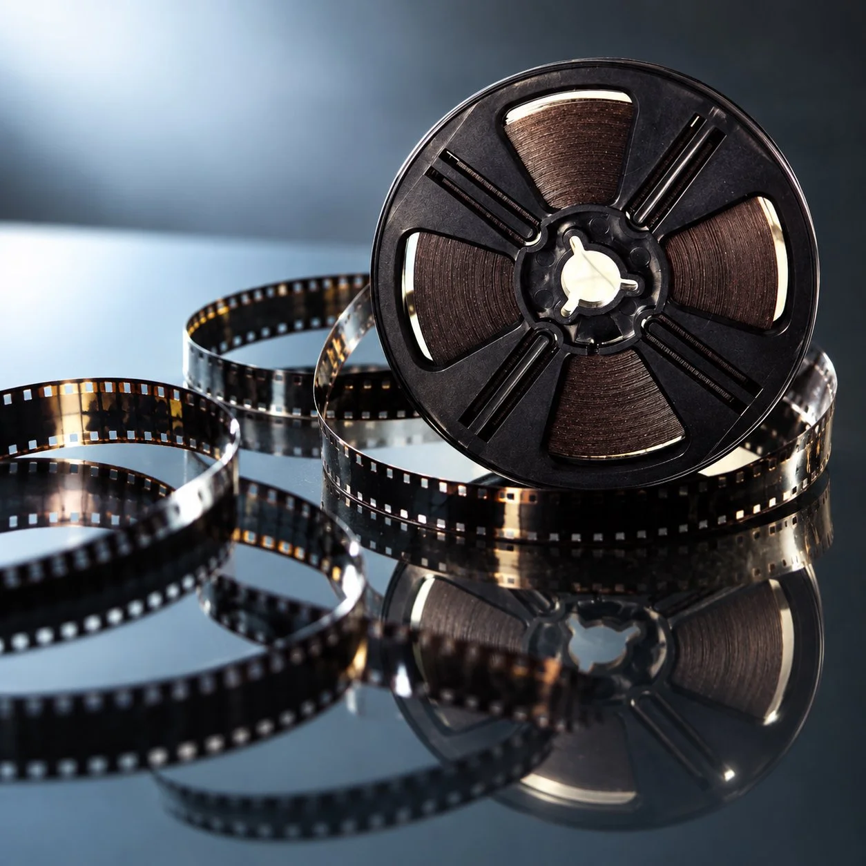 Reel of motion picture film and film strips on a reflective surface.