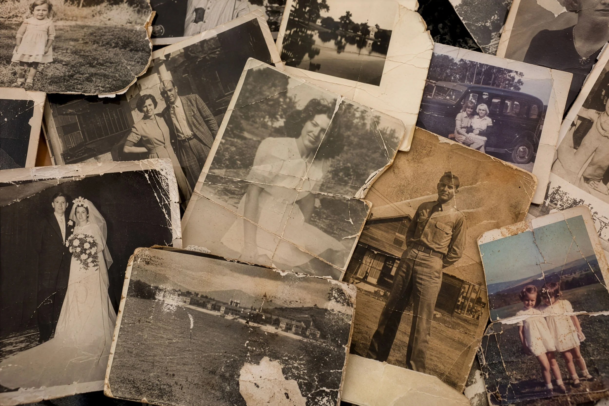 A collection of old, worn black and white photographs featuring children, adults, landscapes, and buildings, some torn and creased.