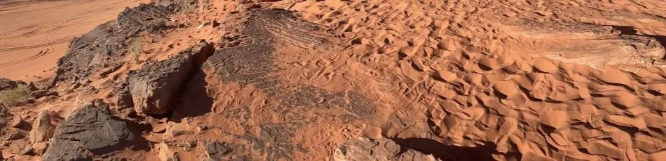 Rugged red sandstone rock formation surrounded by wind-sculpted desert sand dunes