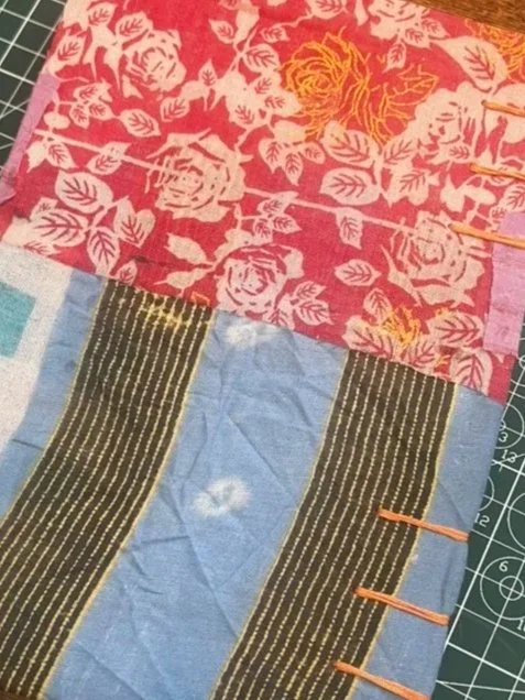 Close-up of a colorful patchwork quilt with red floral fabric, blue sections, and black striped panels on a cutting mat