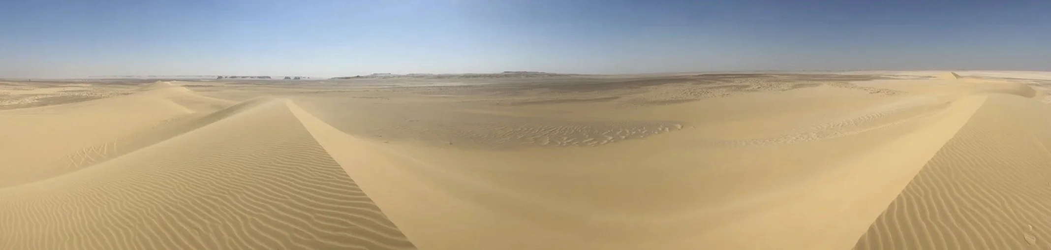 Panoramic view of rippled golden sand dunes stretching across a vast desert under a clear blue sky