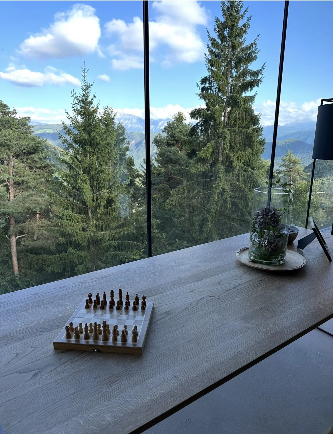 Floor-to-ceiling window at Saltus looking over tall pine trees to the mountains, with a chess board on the table