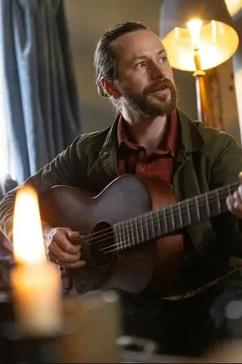 Bearded man playing acoustic guitar in a warmly lit room