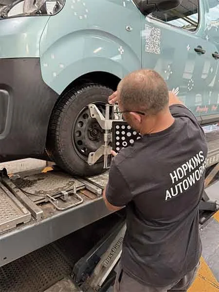 Automotive technician using a wheel alignment tool on a vehicle at a repair shop