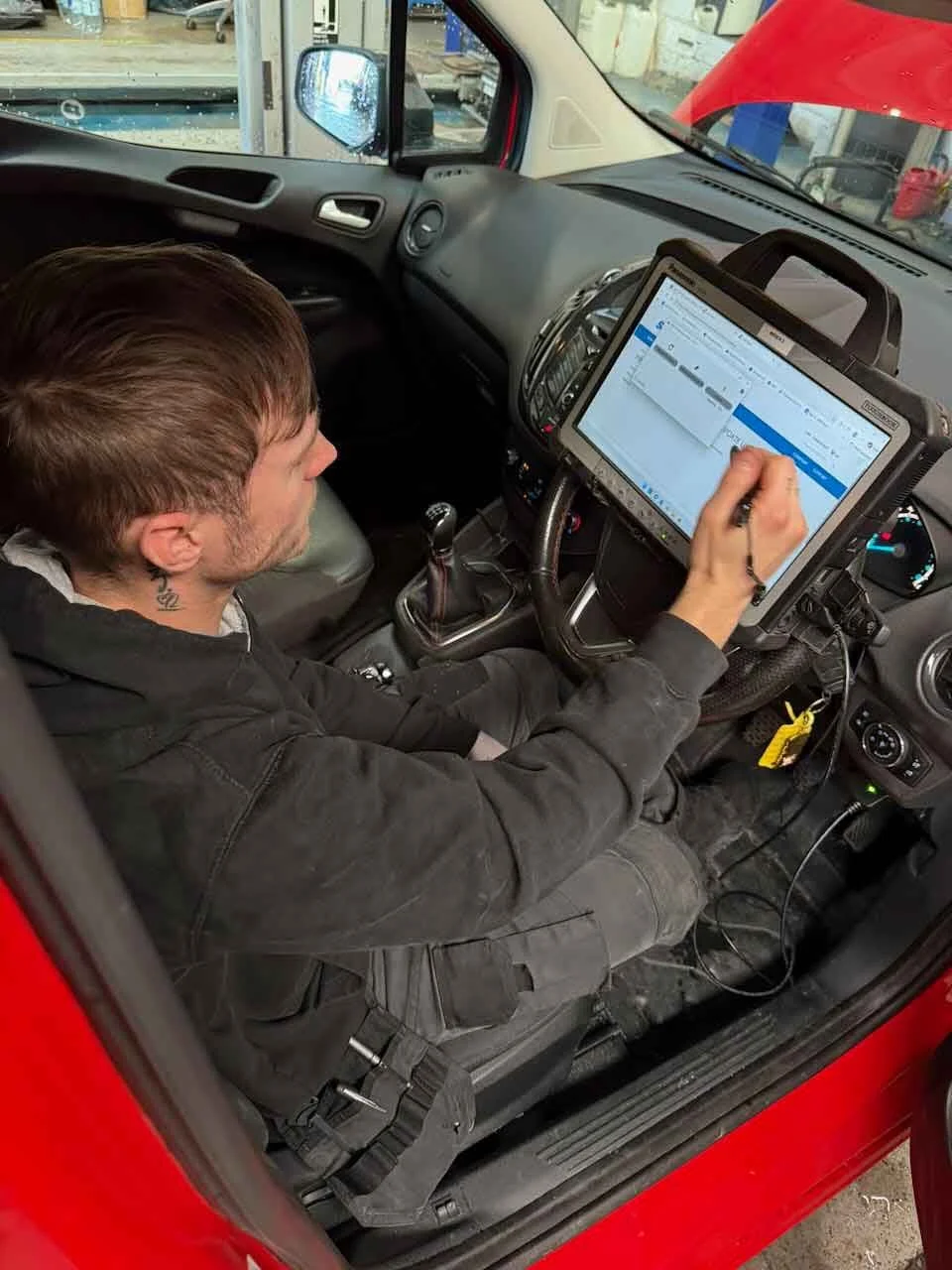 Technician using a diagnostic tablet inside a red car at an auto repair shop