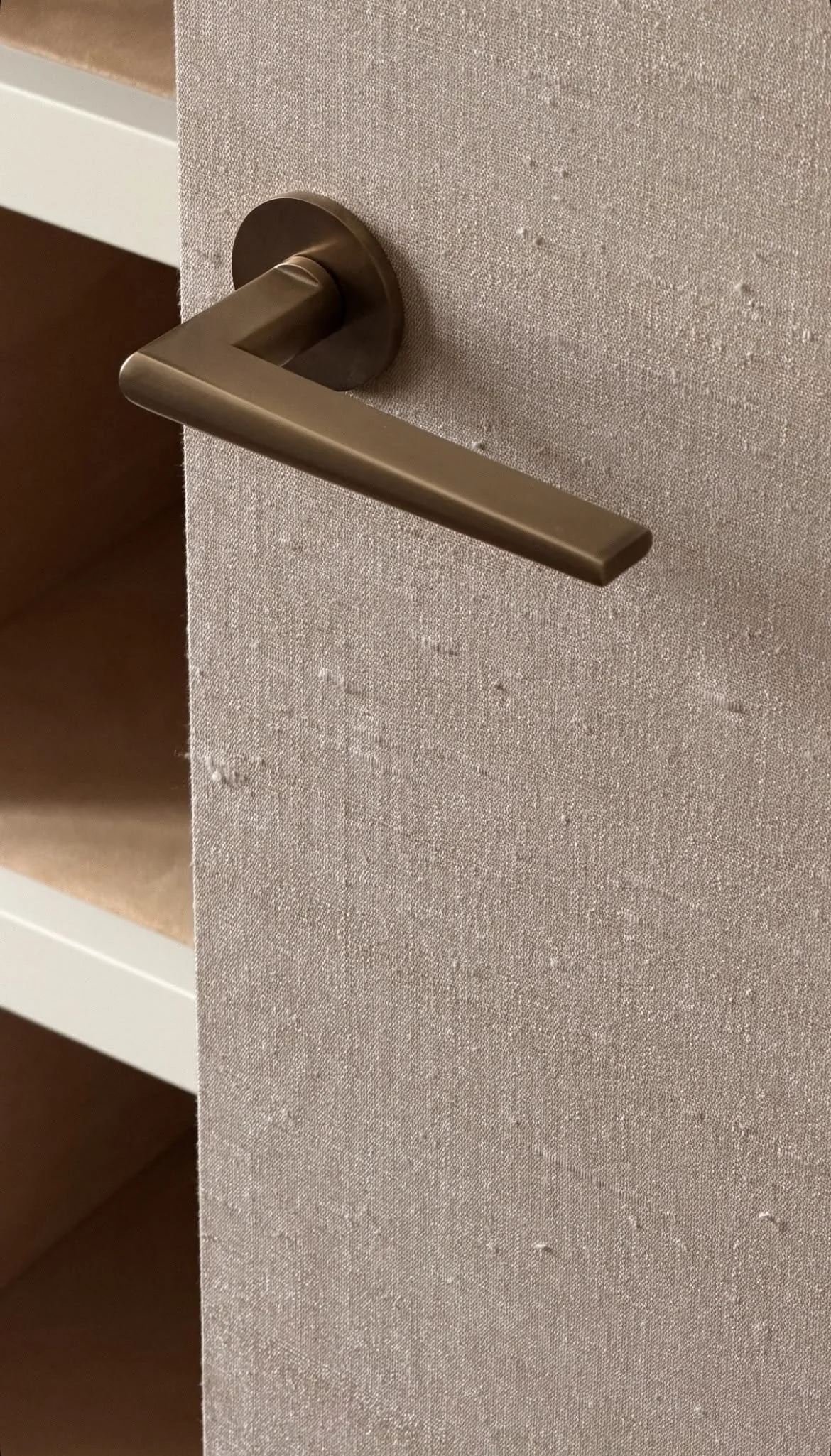 Close-up of a brushed bronze lever door handle on a textured beige door