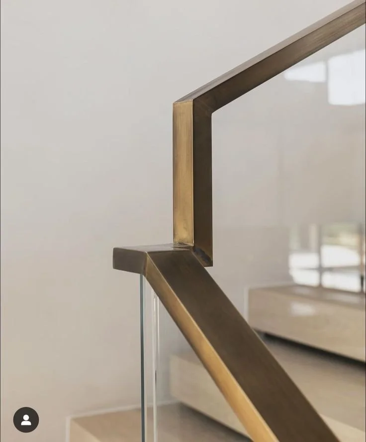Close-up of a modern glass staircase with a dark wood and brass handrail.