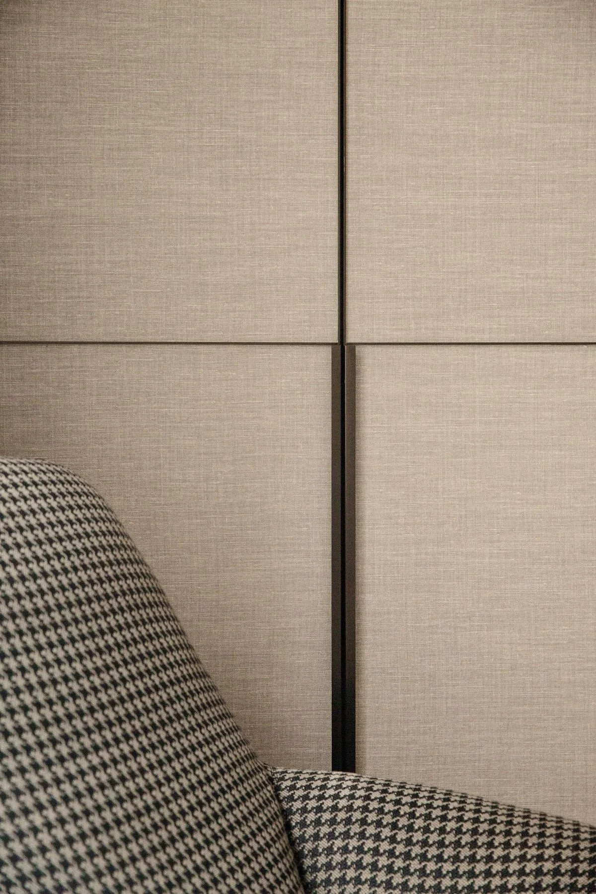 Close-up of a black-and-white houndstooth upholstered chair against beige paneled wall