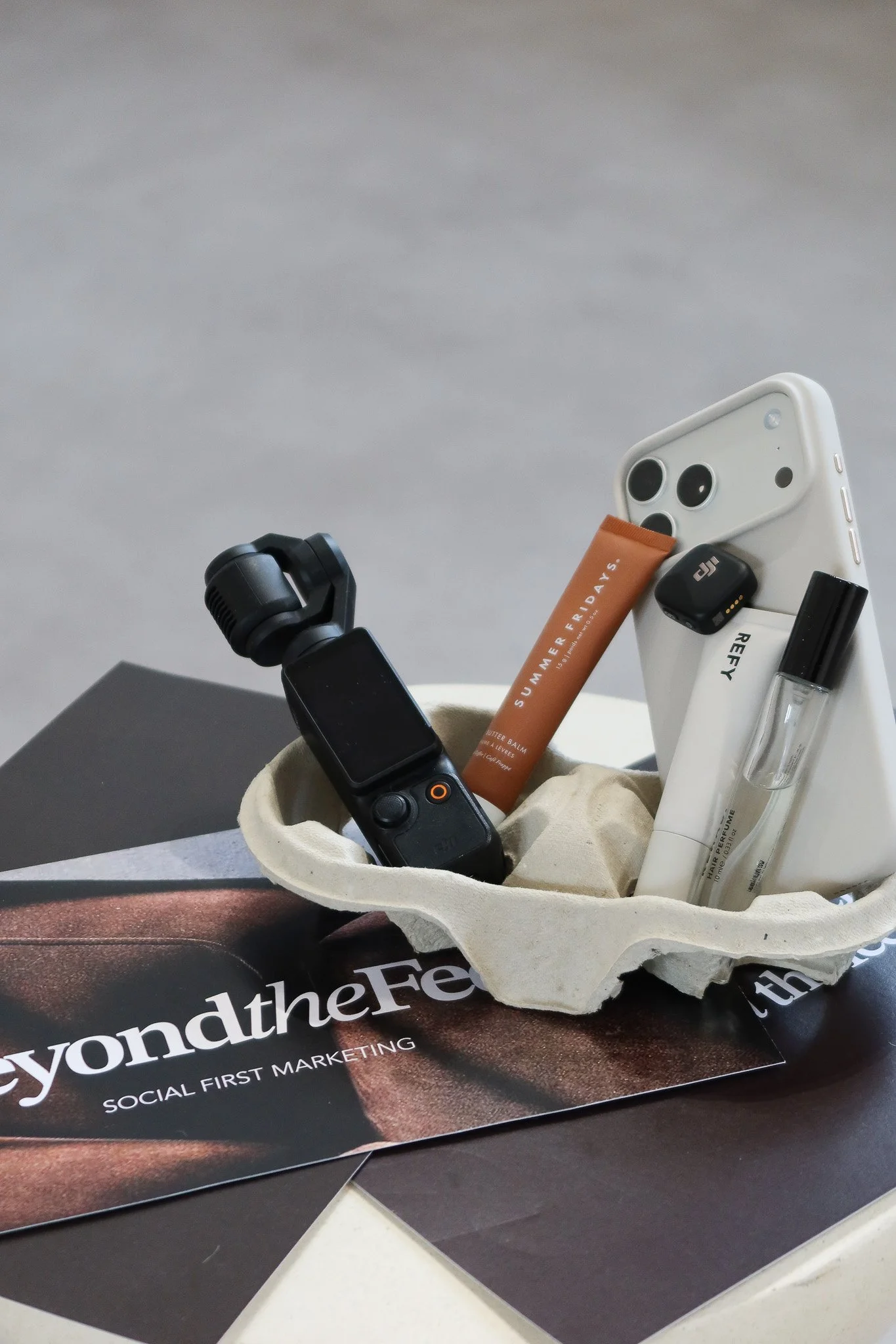 Content creation kit for an event shoot: a gimbal camera, phone, lipstick and lip gloss in a coffee cup carrier on Beyond The Feed cards