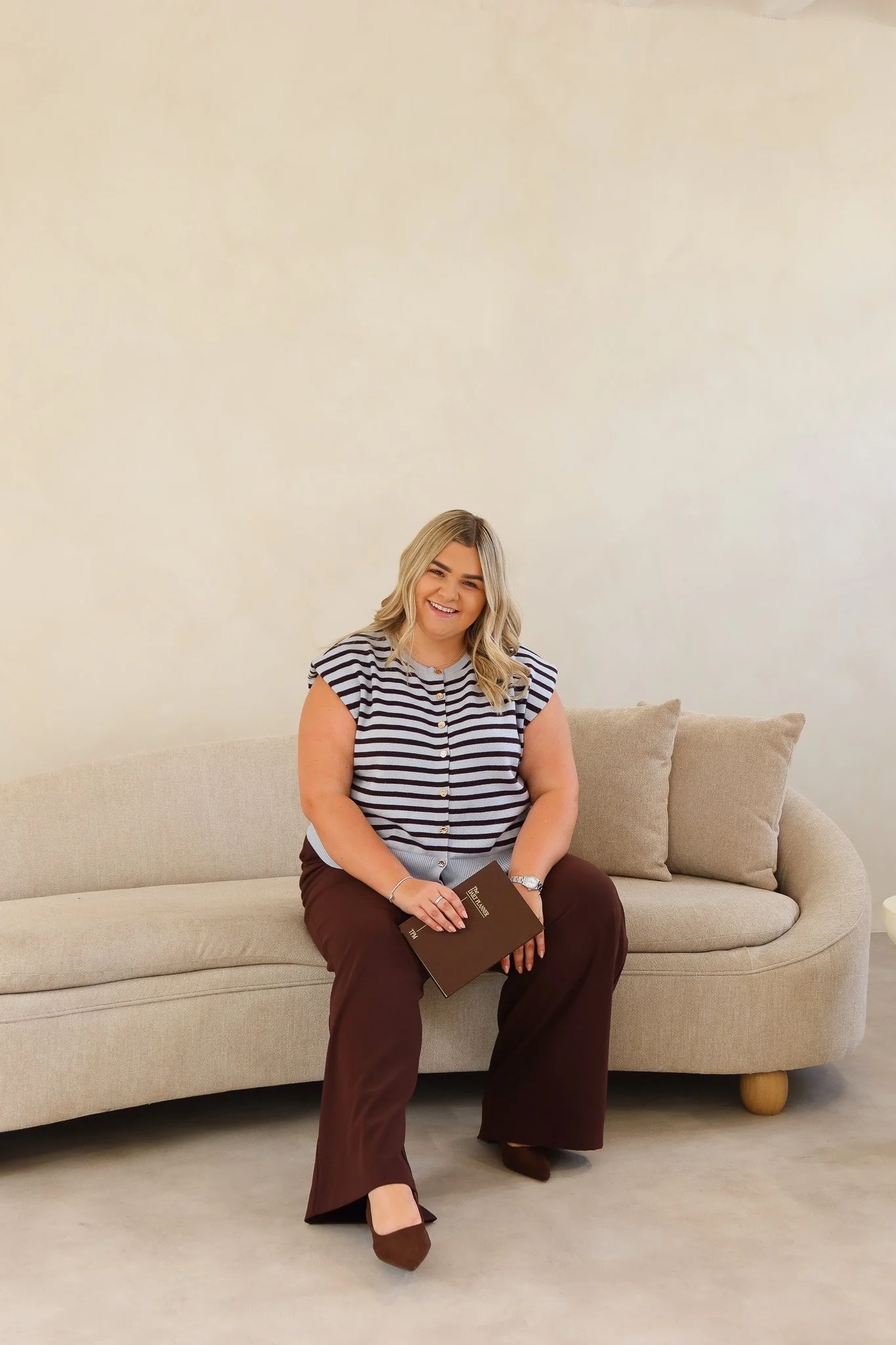 Lauren from Beyond The Feed in a blue striped top and brown trousers, sitting on a cream sofa