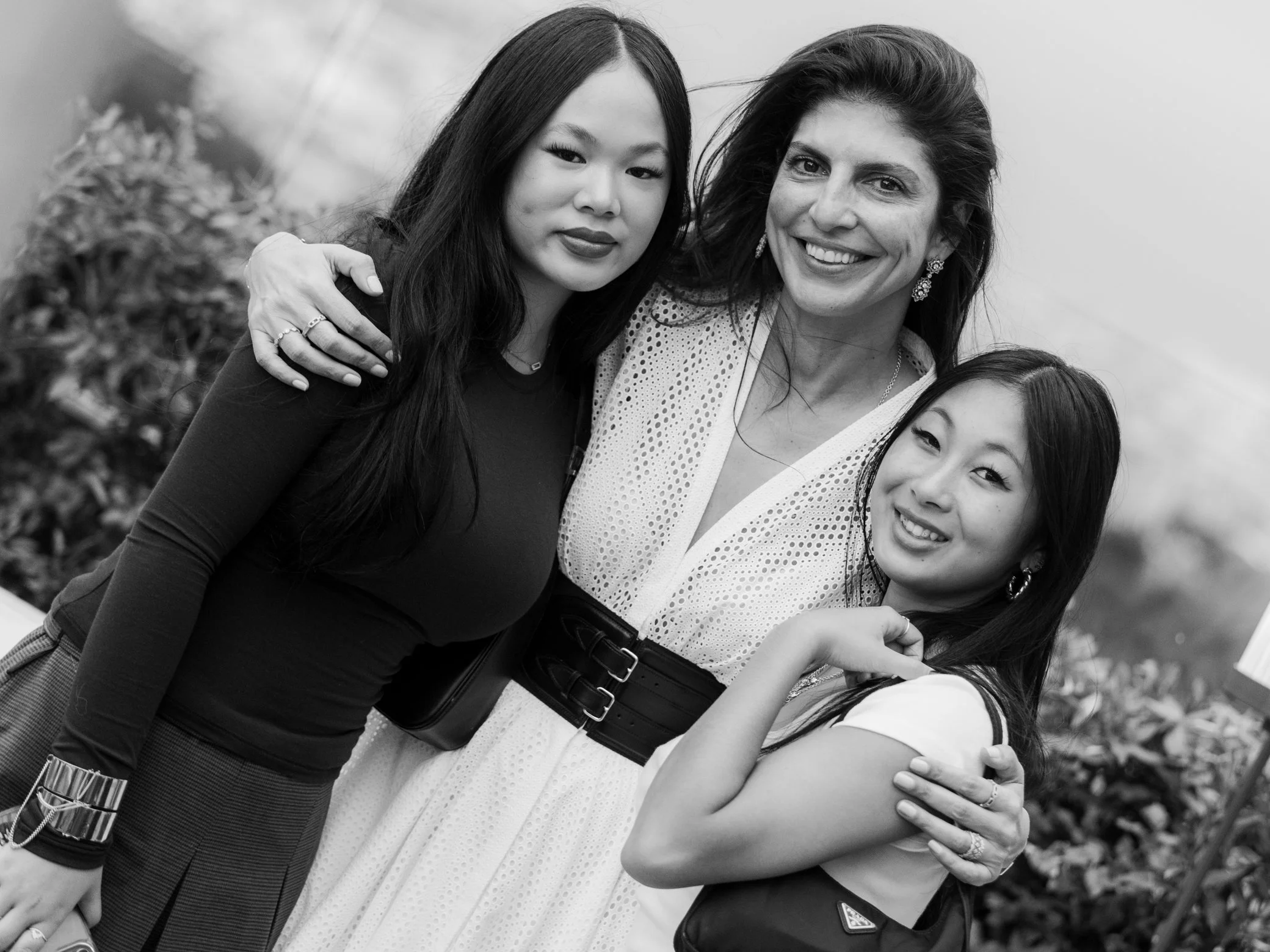 Portrait en noir et blanc de trois femmes souriantes posant ensemble, bras dessus bras dessous.