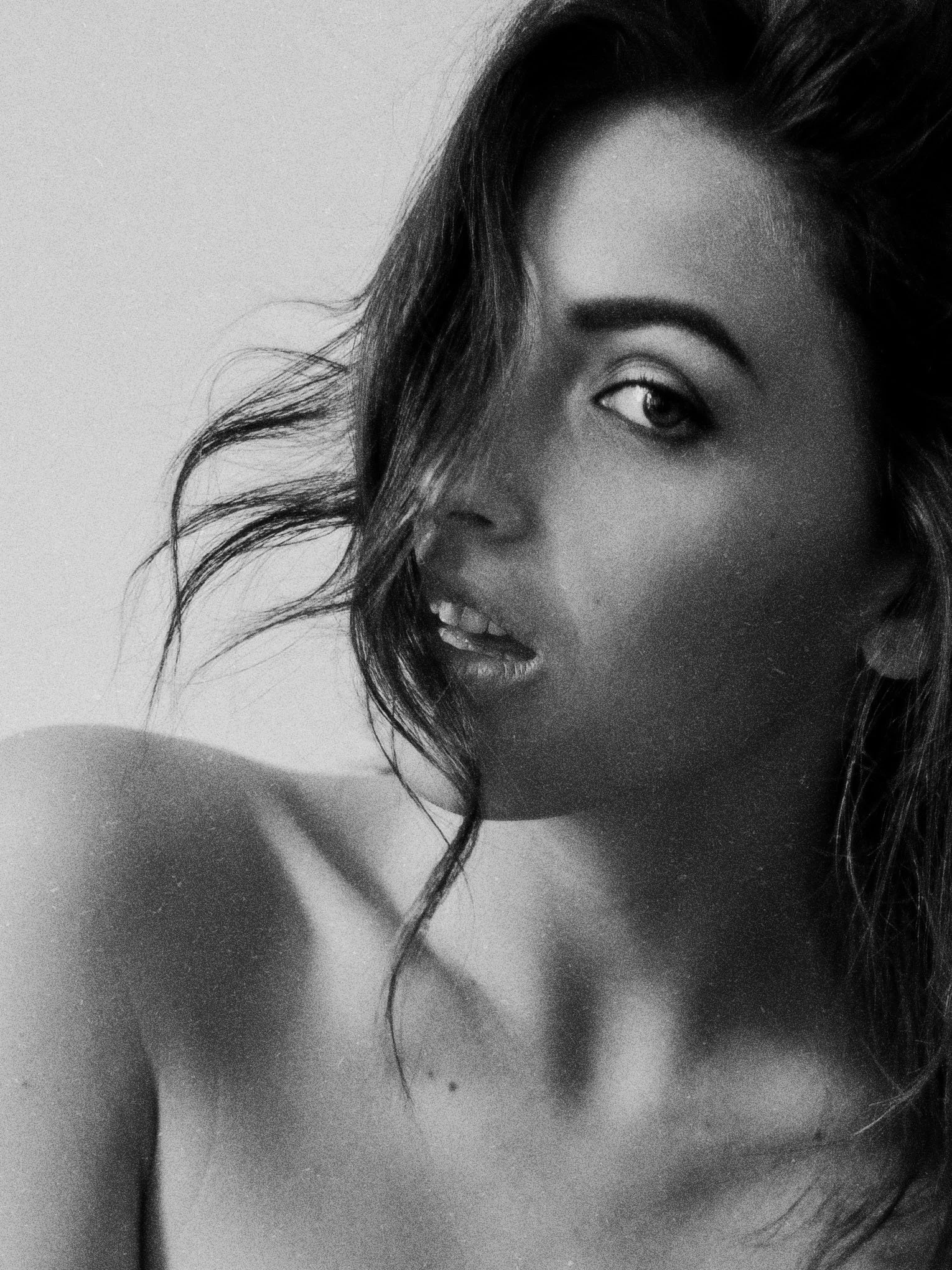 Portrait en gros plan en noir et blanc d’une femme souriante aux cheveux longs, regardant l’objectif.