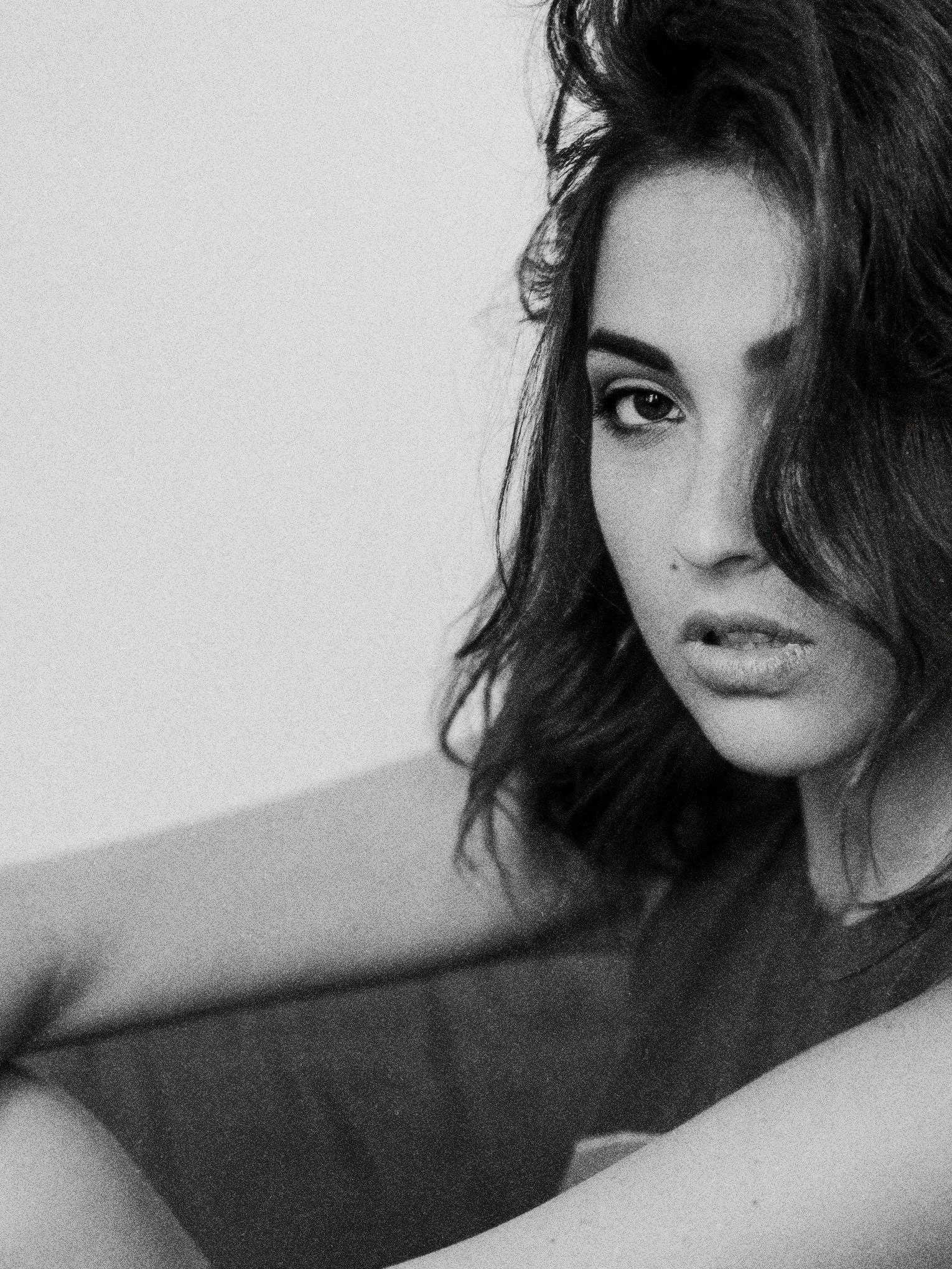 Portrait en noir et blanc d’une femme aux cheveux longs, regardant l’objectif, avec un espace négatif à gauche.