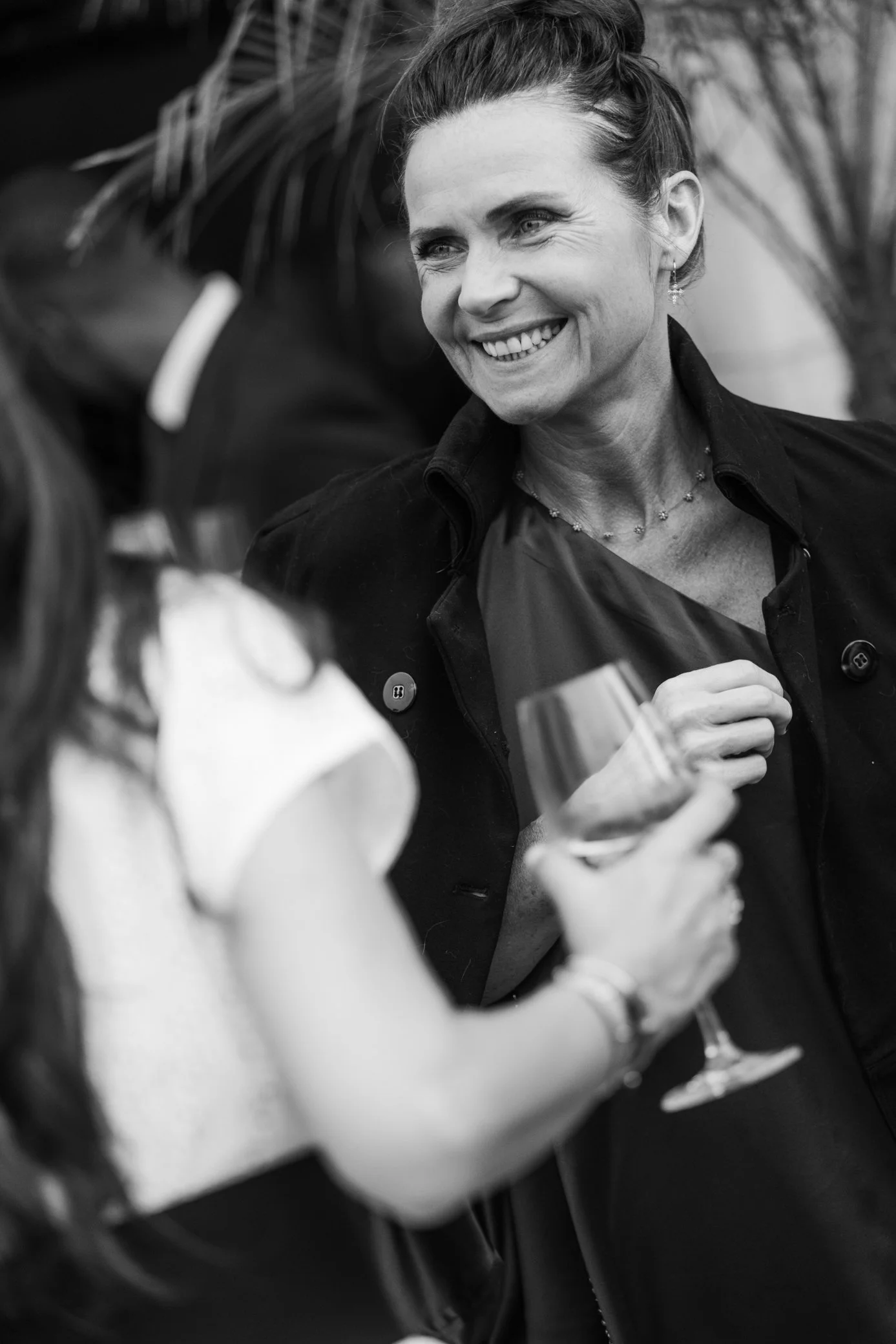 Portrait en noir et blanc d’une femme souriante tenant une coupe de champagne lors d’un événement.