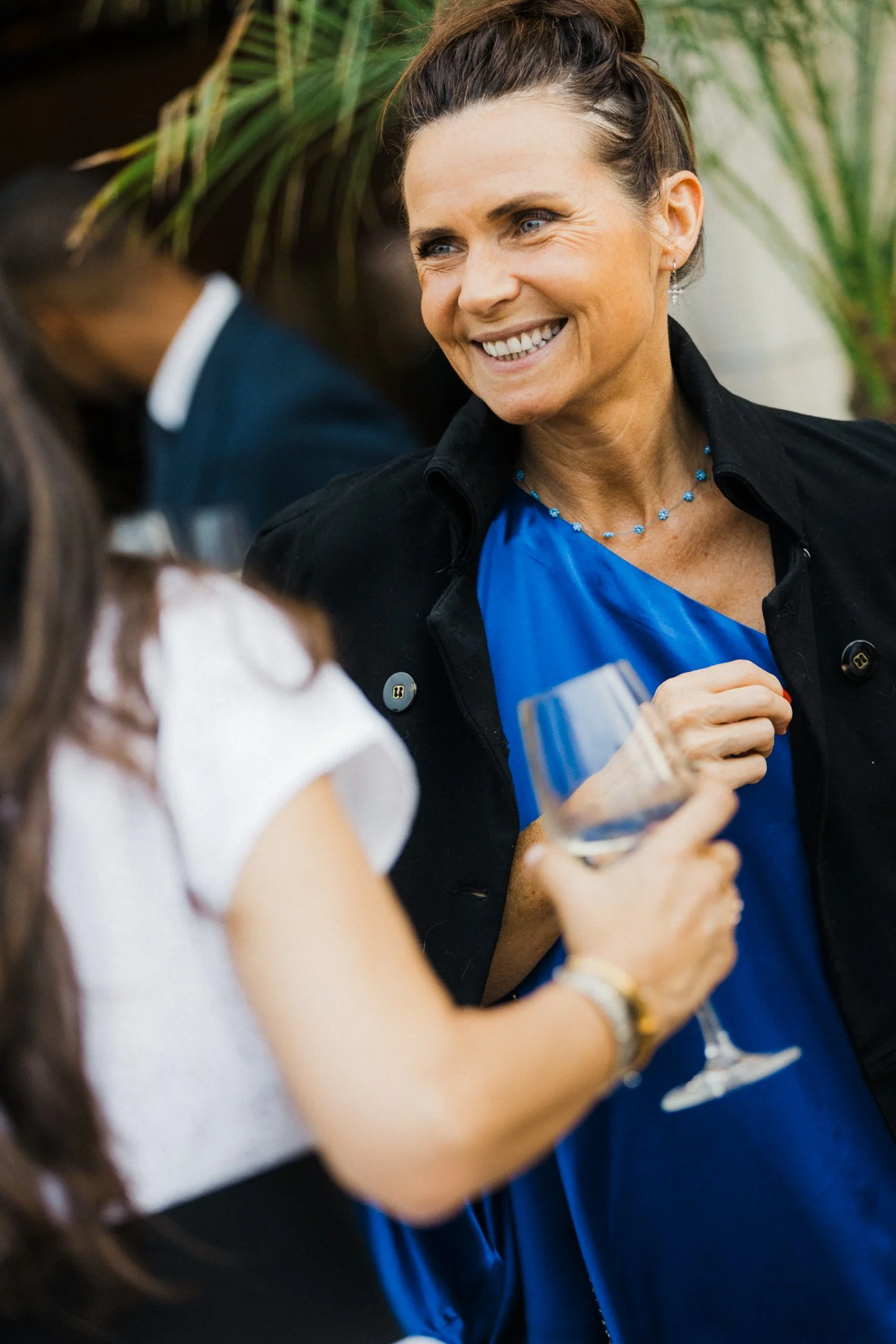 Femme souriante en robe bleue et veste noire tenant une coupe lors d’un événement