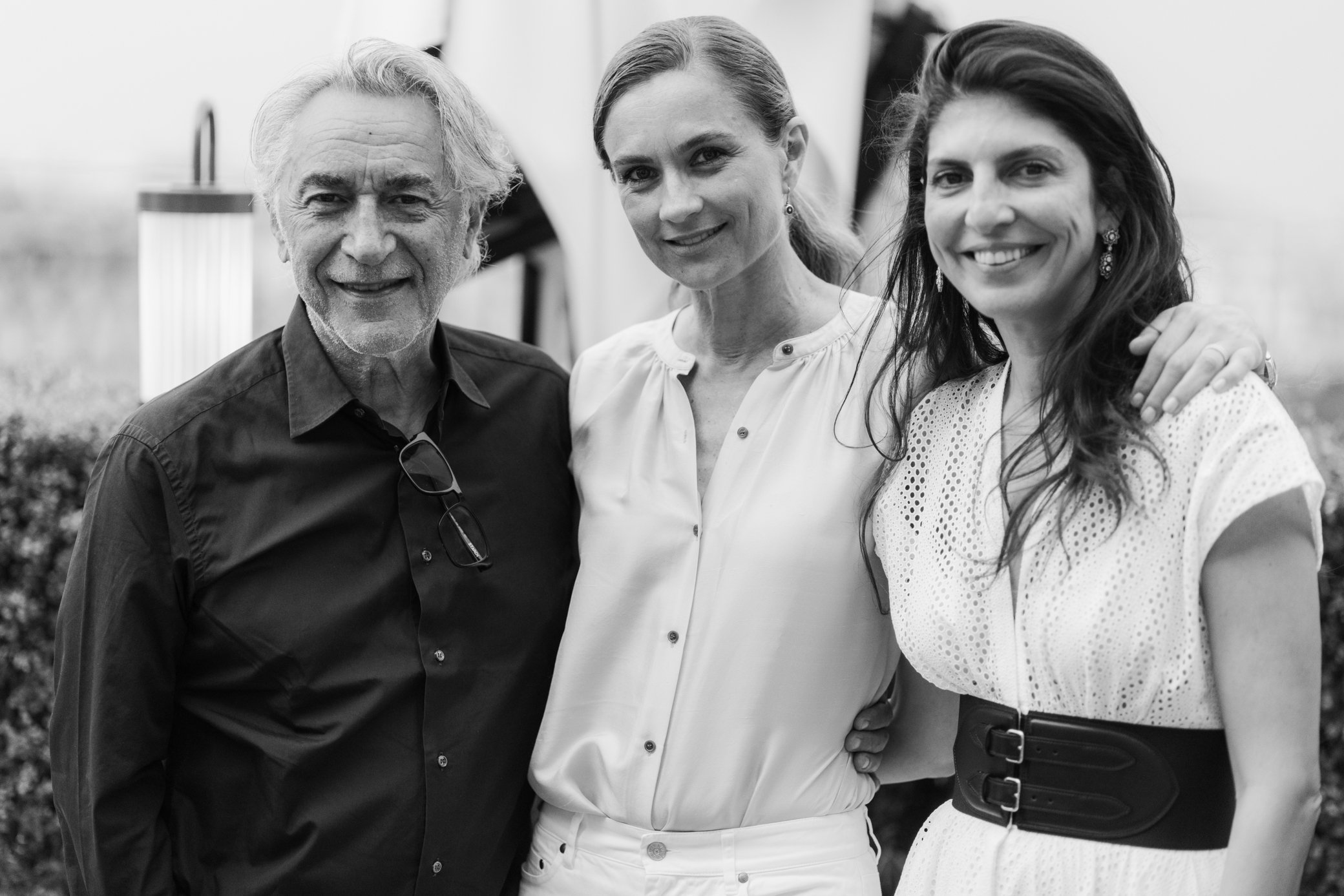 Portrait en noir et blanc de trois personnes souriantes posant ensemble en extérieur.