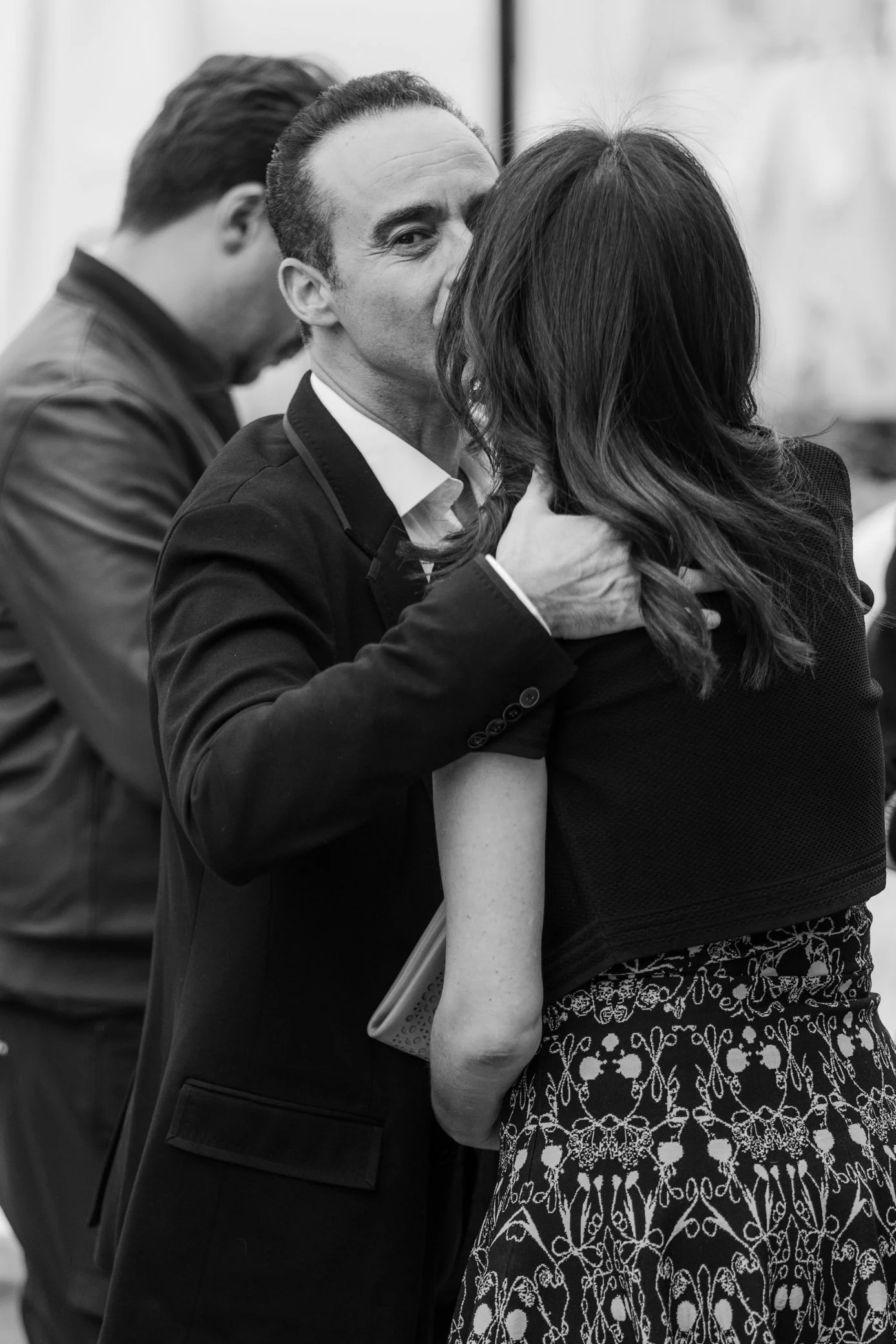 Photo en noir et blanc d’un homme en costume embrassant une femme aux cheveux longs lors d’un événement.