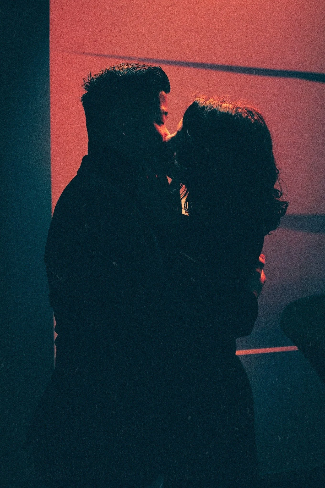 Silhouettes d’un couple s’embrassant devant un mur éclairé de rouge.