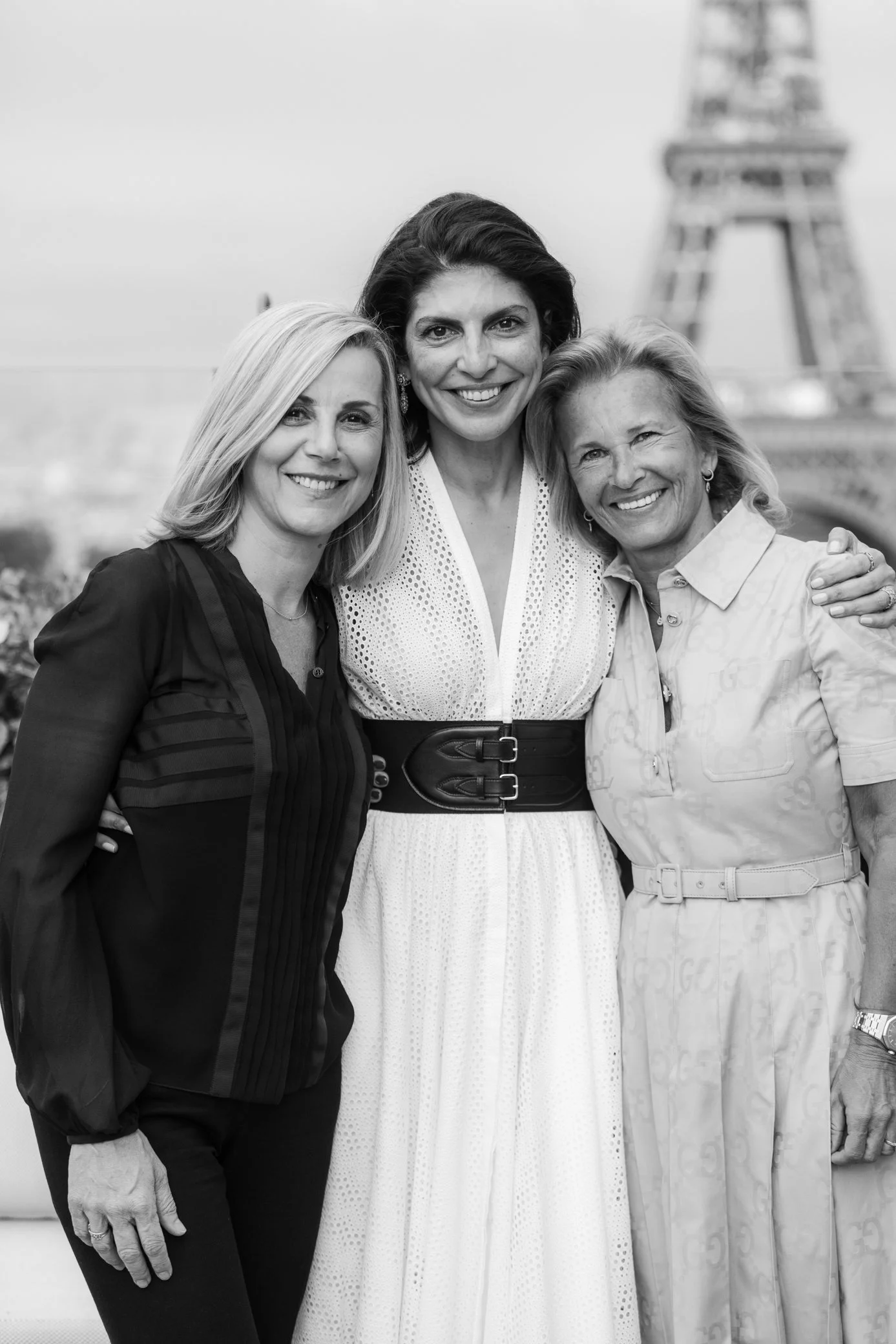 Portrait en noir et blanc de trois femmes souriantes devant la tour Eiffel à Paris.