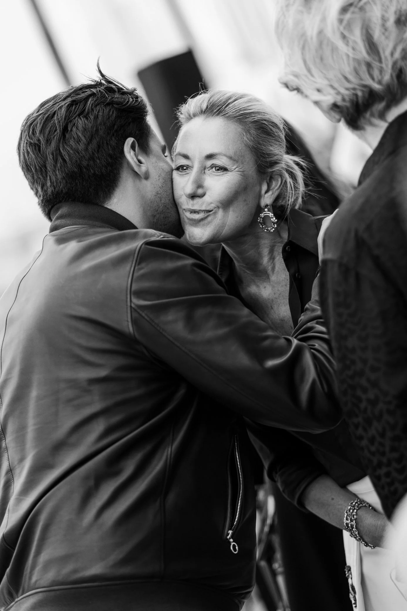 Photo en noir et blanc d’un homme embrassant une femme sur la joue lors d’une réception, entourés d’autres invités.