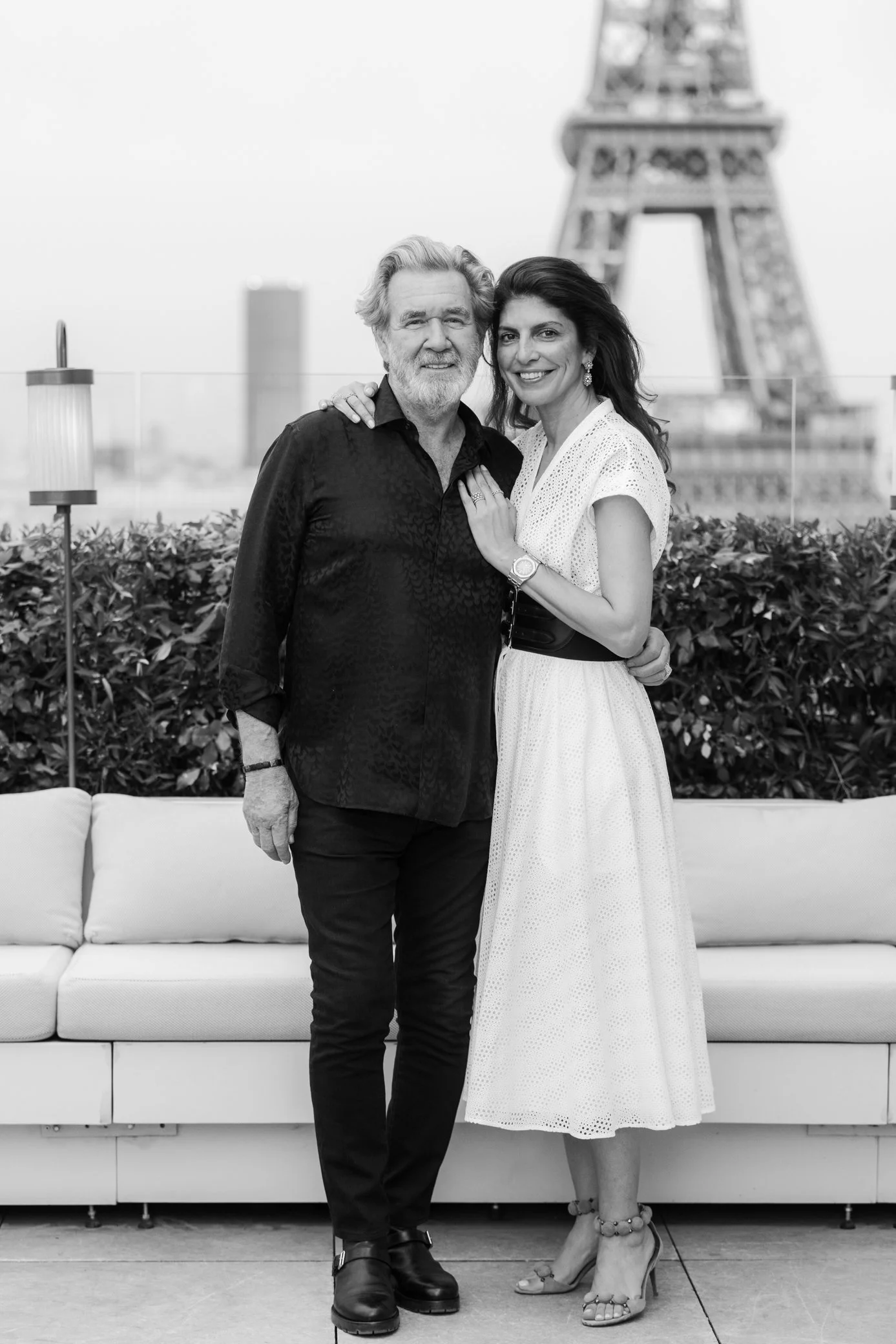 Portrait en noir et blanc d’un couple posant devant la tour Eiffel, un canapé blanc en arrière-plan.