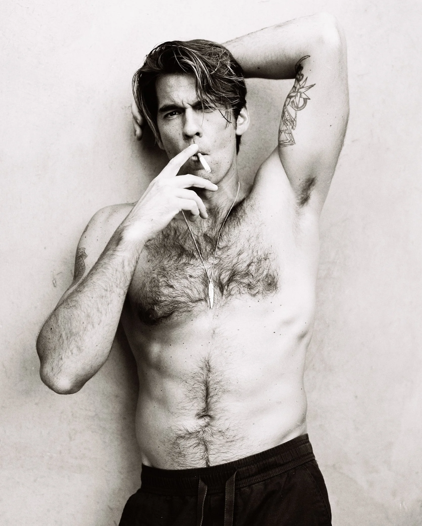 Portrait en noir et blanc d’un homme torse nu, tatoué, fumant une cigarette.