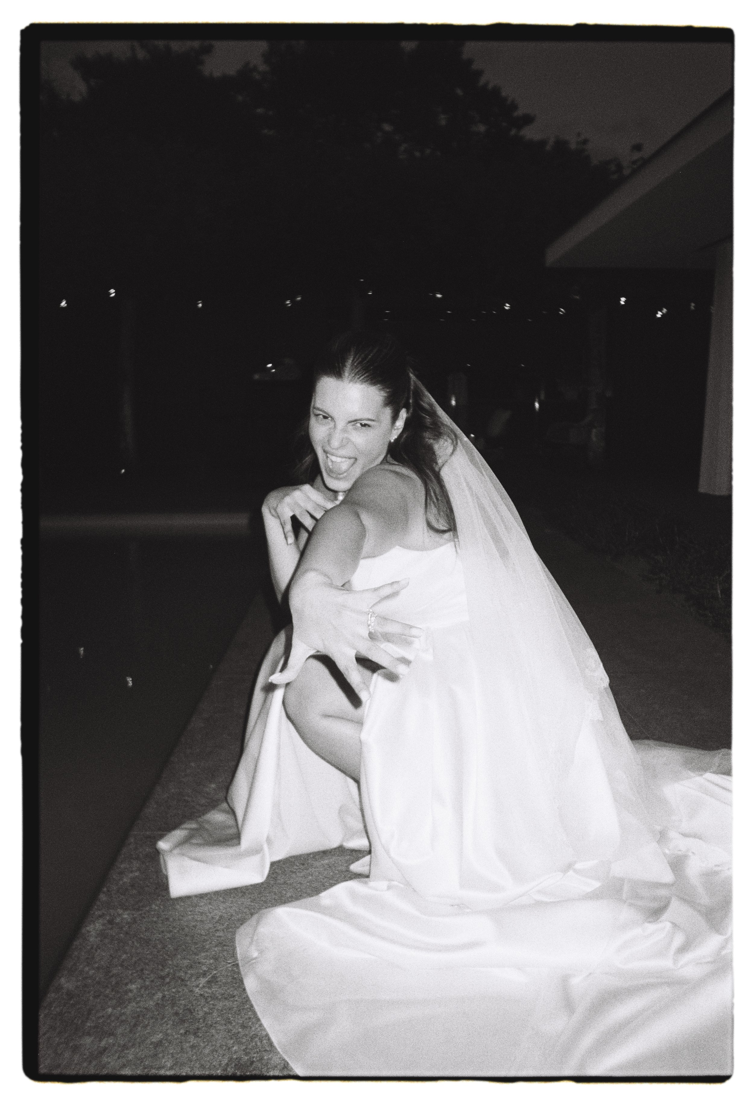 Mariée souriante en robe blanche et voile, photographiée en noir et blanc lors d’une cérémonie nocturne.