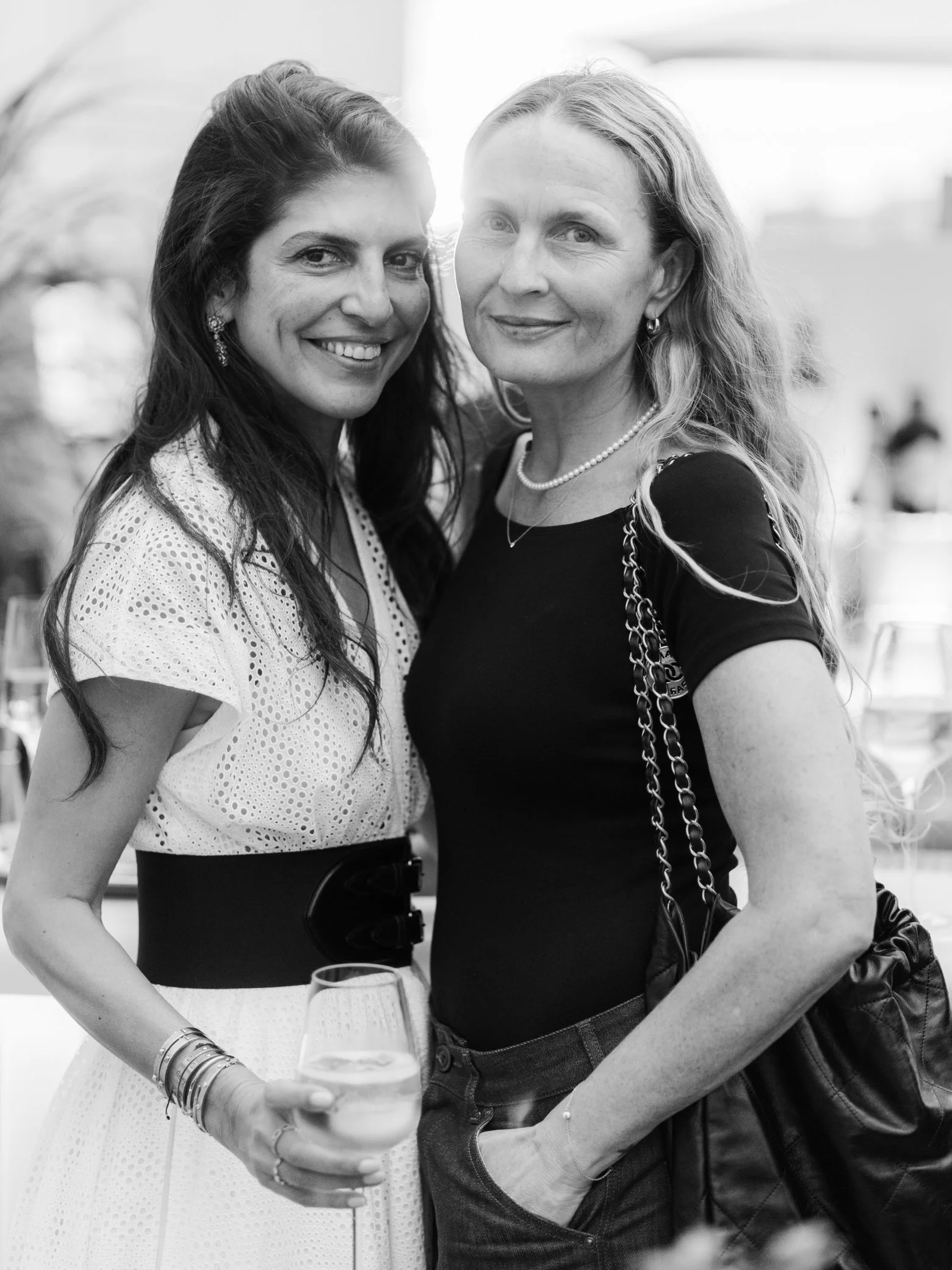 Portrait en noir et blanc de deux femmes souriantes lors d’un événement, l’une tenant un verre.