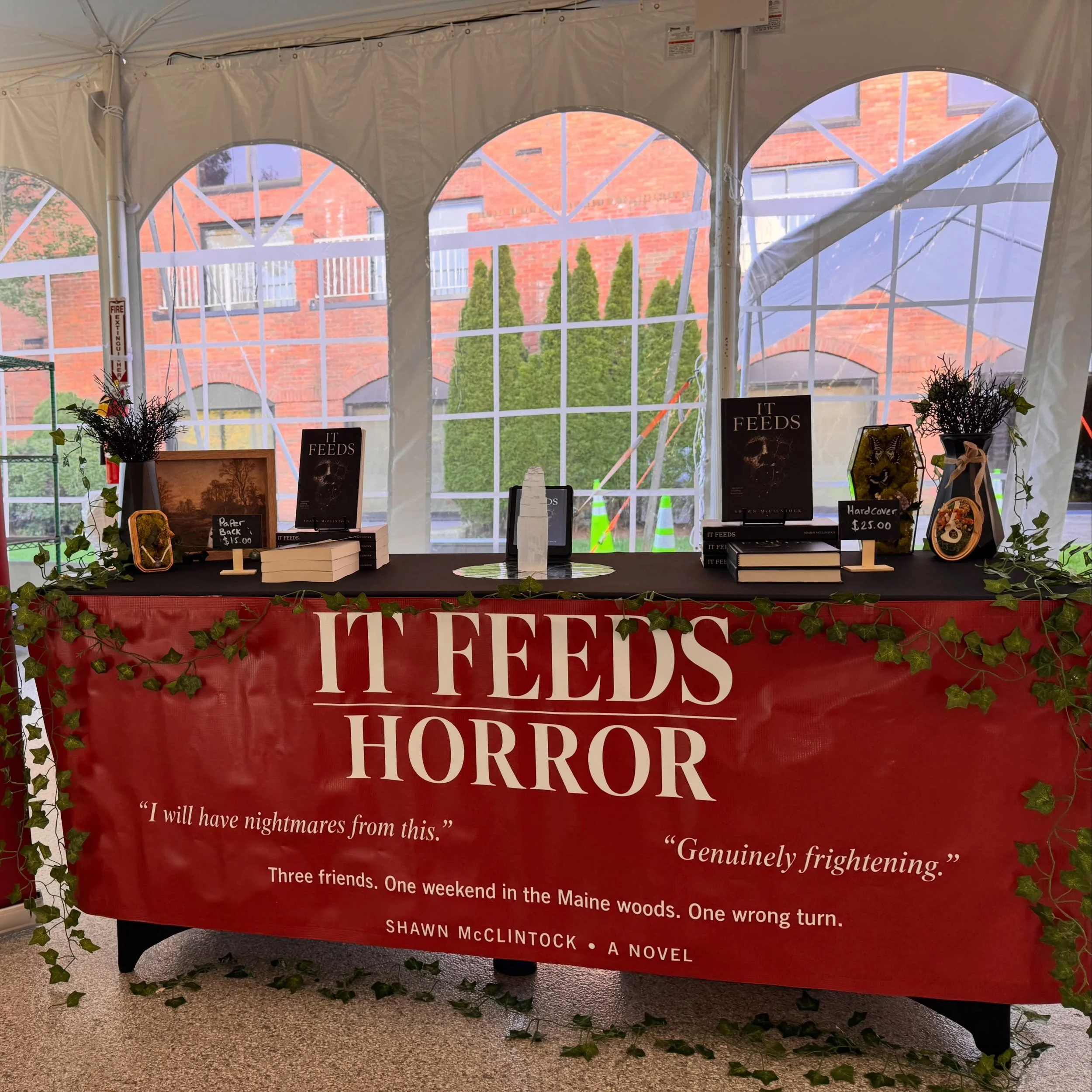 Book display for Shawn McClintock’s horror novel “It Feeds,” decorated with ivy, horror-themed artwork, and promotional signage.