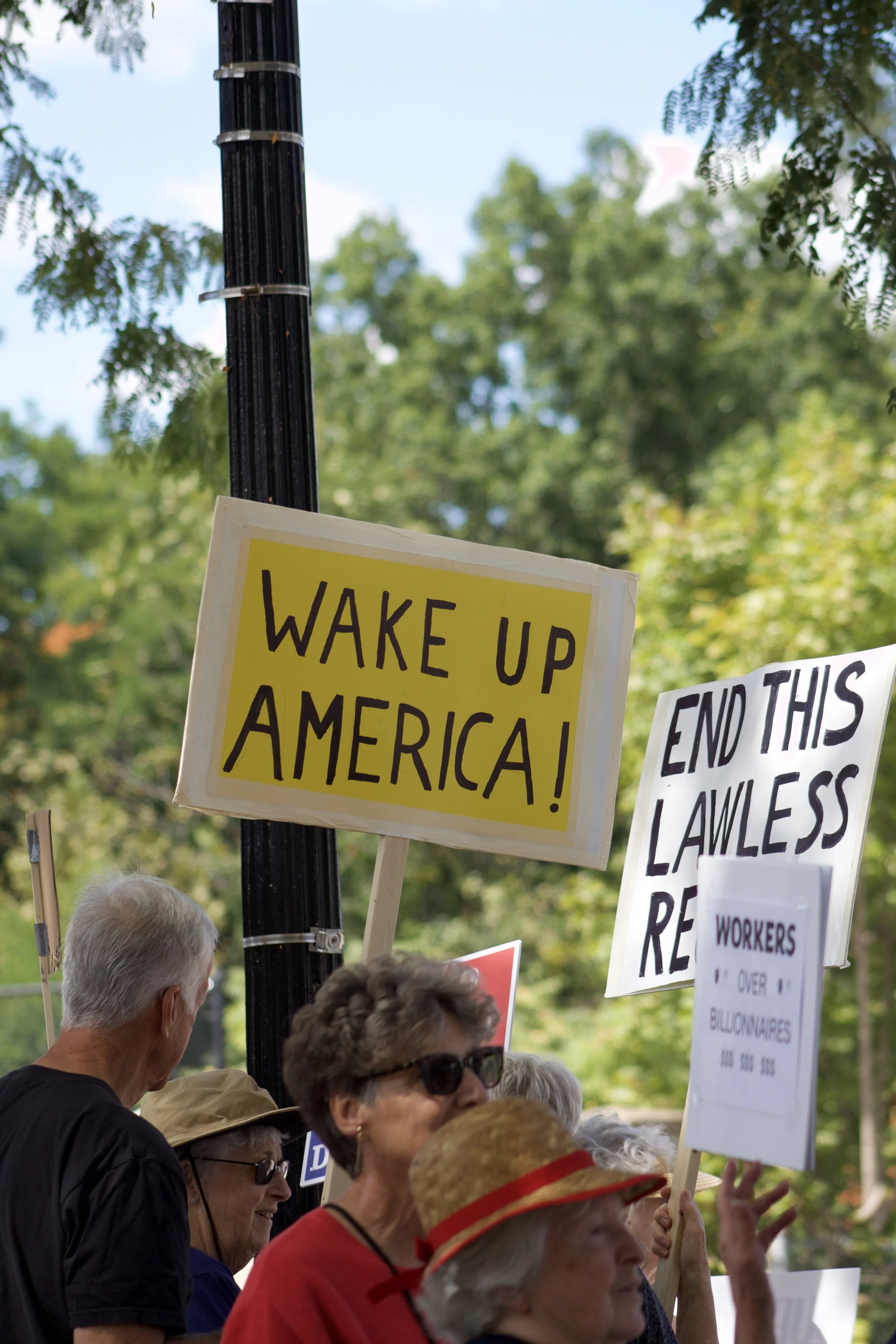 Protesters hold up signs reading "Wake Up America," "Workers Over Billionaires," and "End This Lawless Reform" during a No King's Protest in Kent, Ohio.