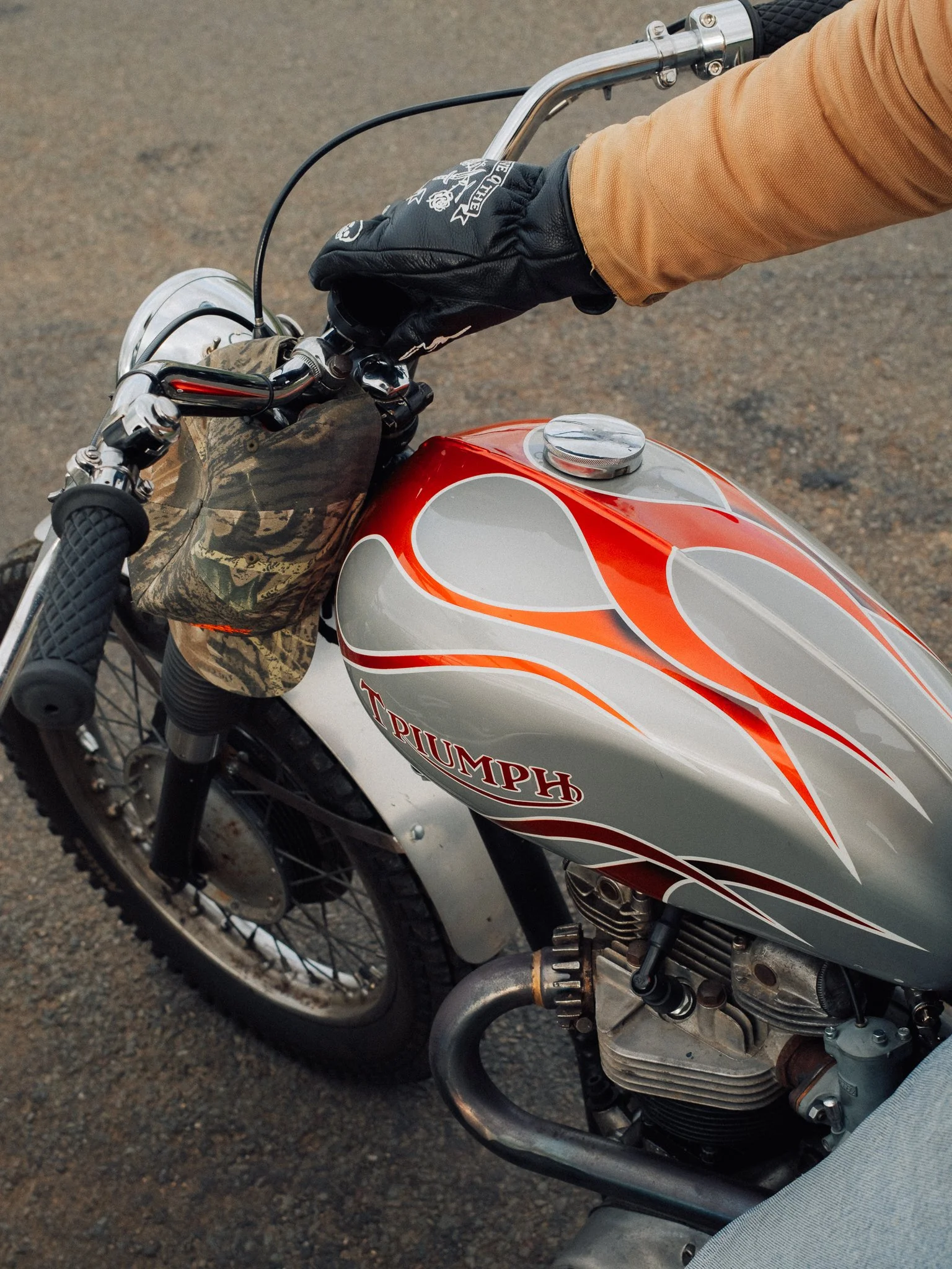Close-up of a rider’s gloved hand on the handlebars of a vintage Triumph motorcycle with a red-and-silver fuel tank.