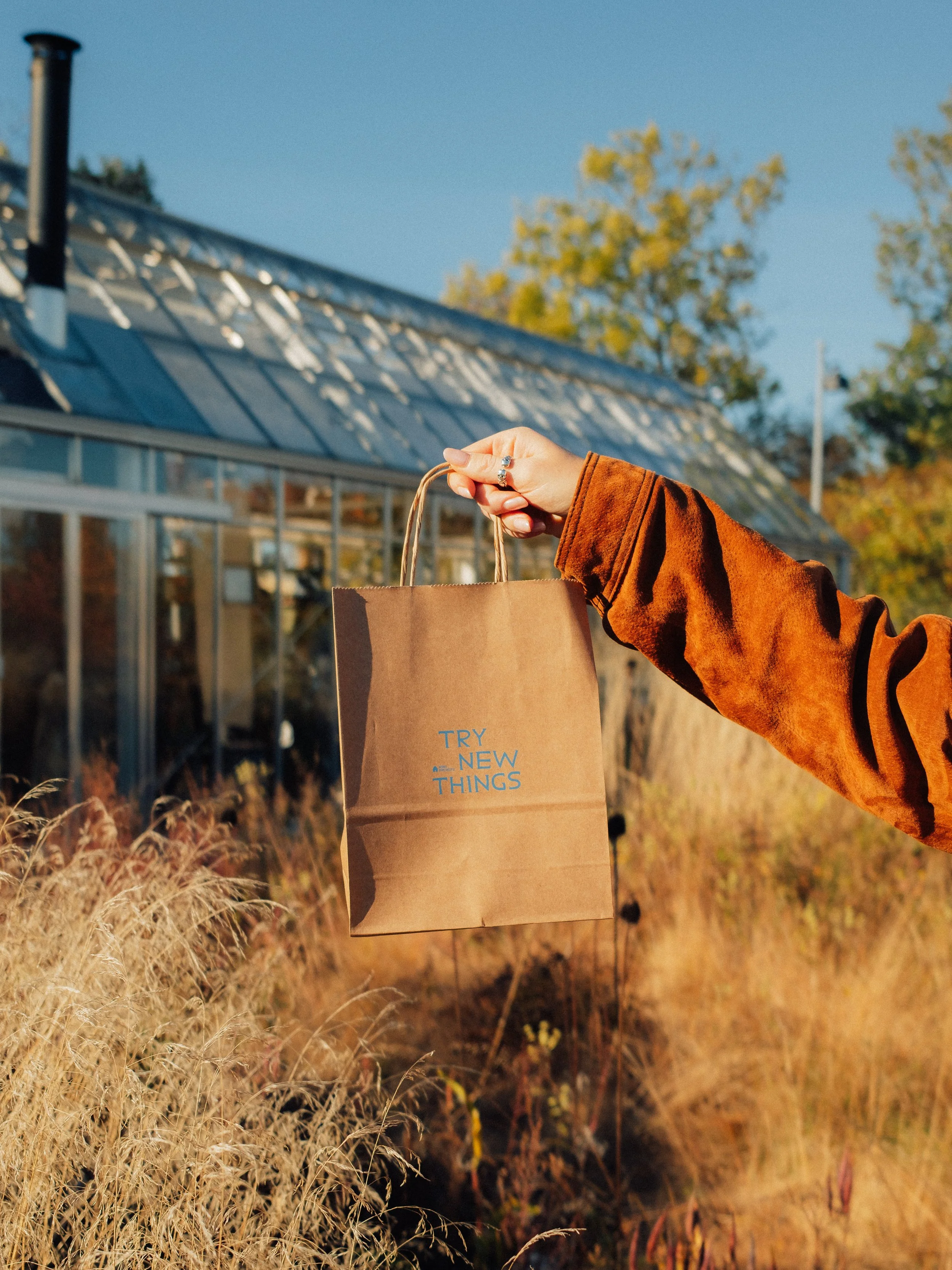 Person in a rust-colored coat carrying a brown paper shopping bag outdoors in autumn.