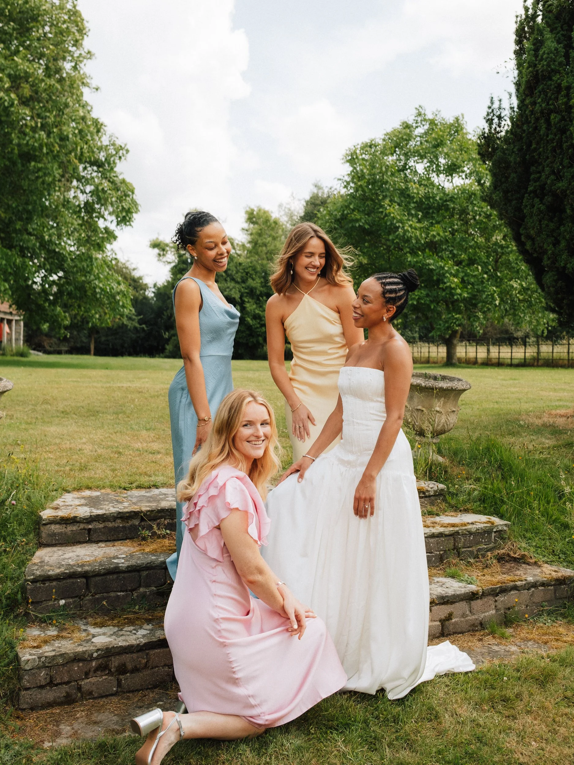 Four women in colorful dresses pose and smile together in a garden.