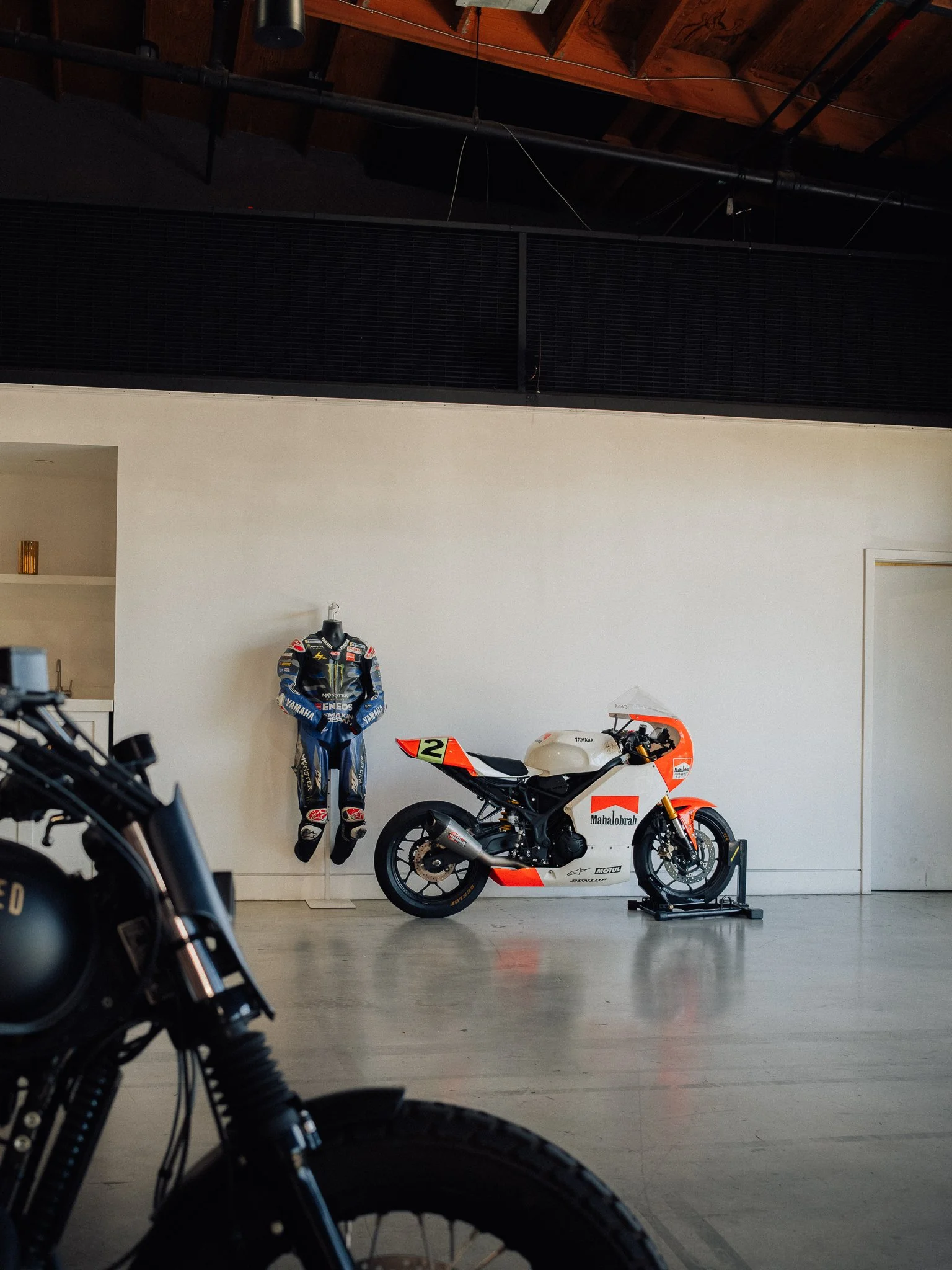 Yamaha racing motorcycle displayed beside a blue Monster Energy racing suit in a modern showroom