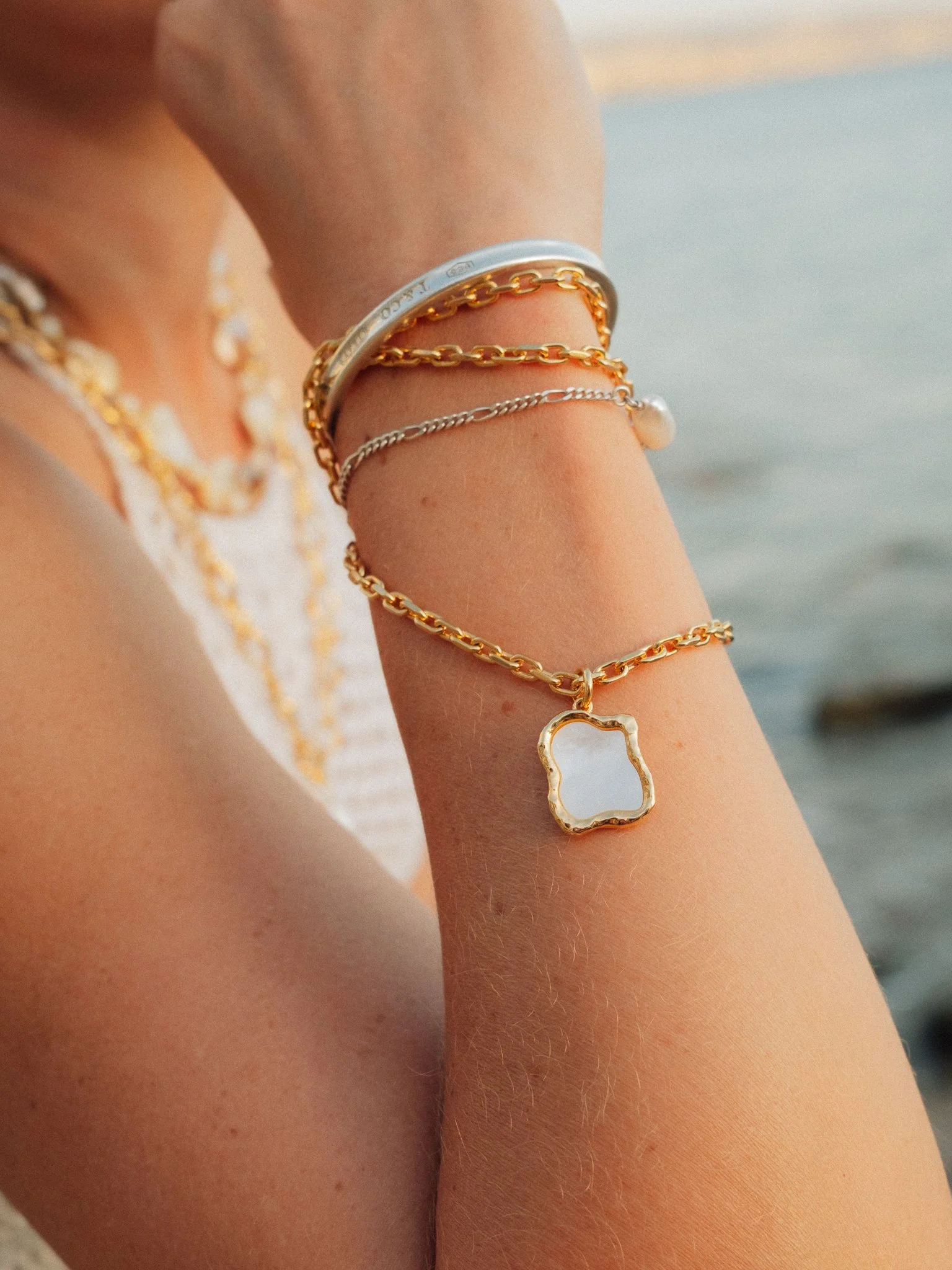 Close-up of a wrist wearing layered gold and silver chain bracelets, including a heart-shaped pendant.