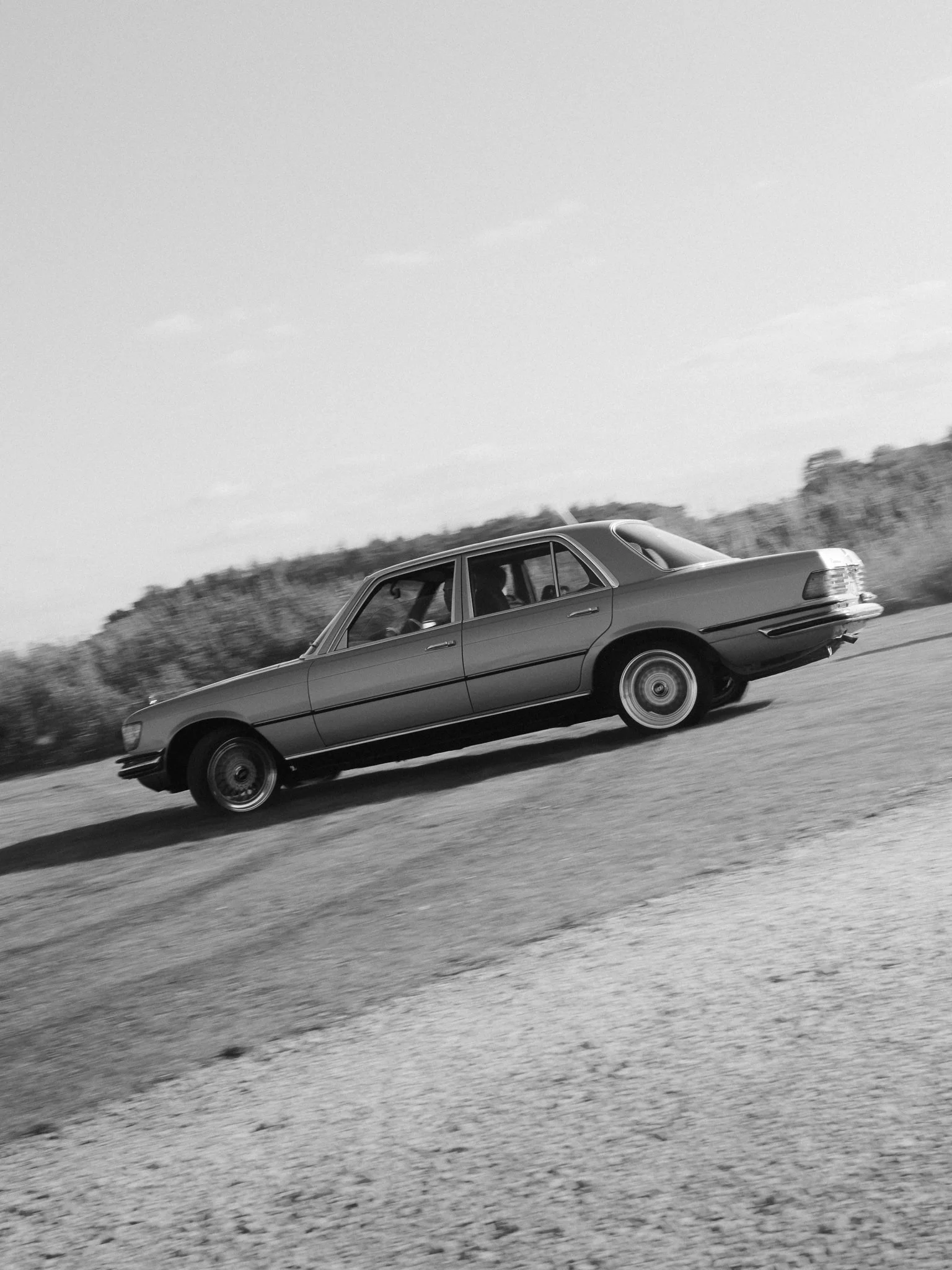 Black-and-white side view of a vintage Mercedes-Benz sedan driving on a road