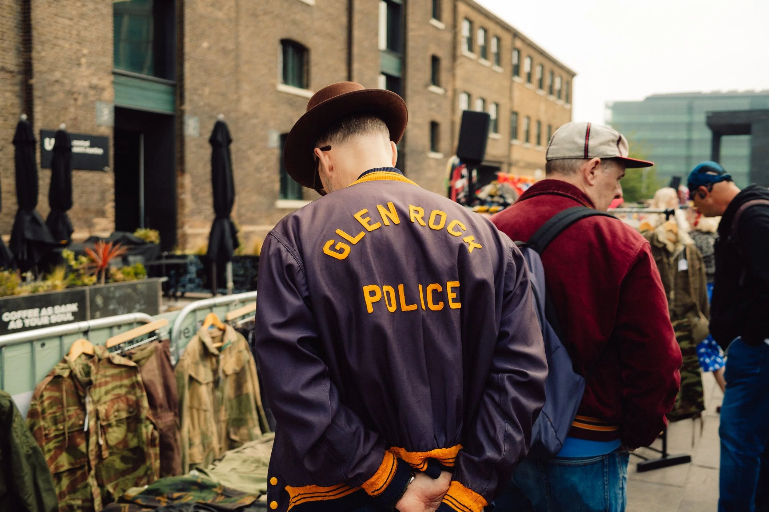 Crowd at an outdoor market with a man wearing a jacket labeled Glenrothes Police in the foreground