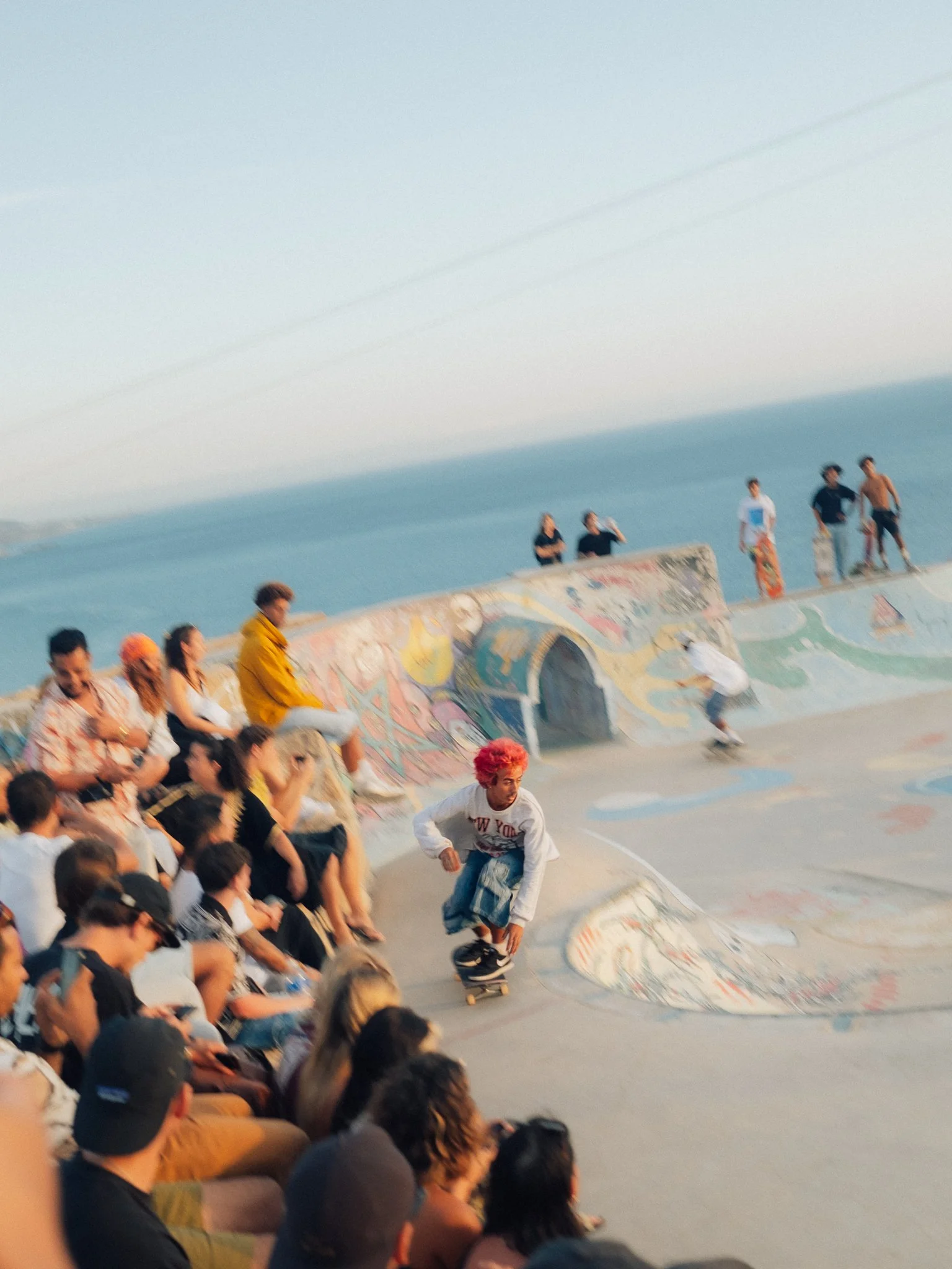 Skateboarder riding through a graffiti-covered outdoor skatepark as a crowd watches.