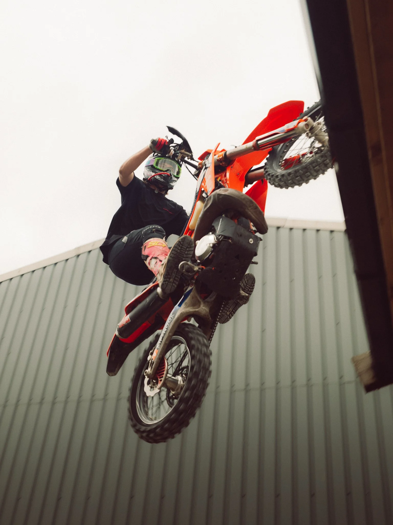 Motocross rider performing a wheelie on an orange dirt bike indoors