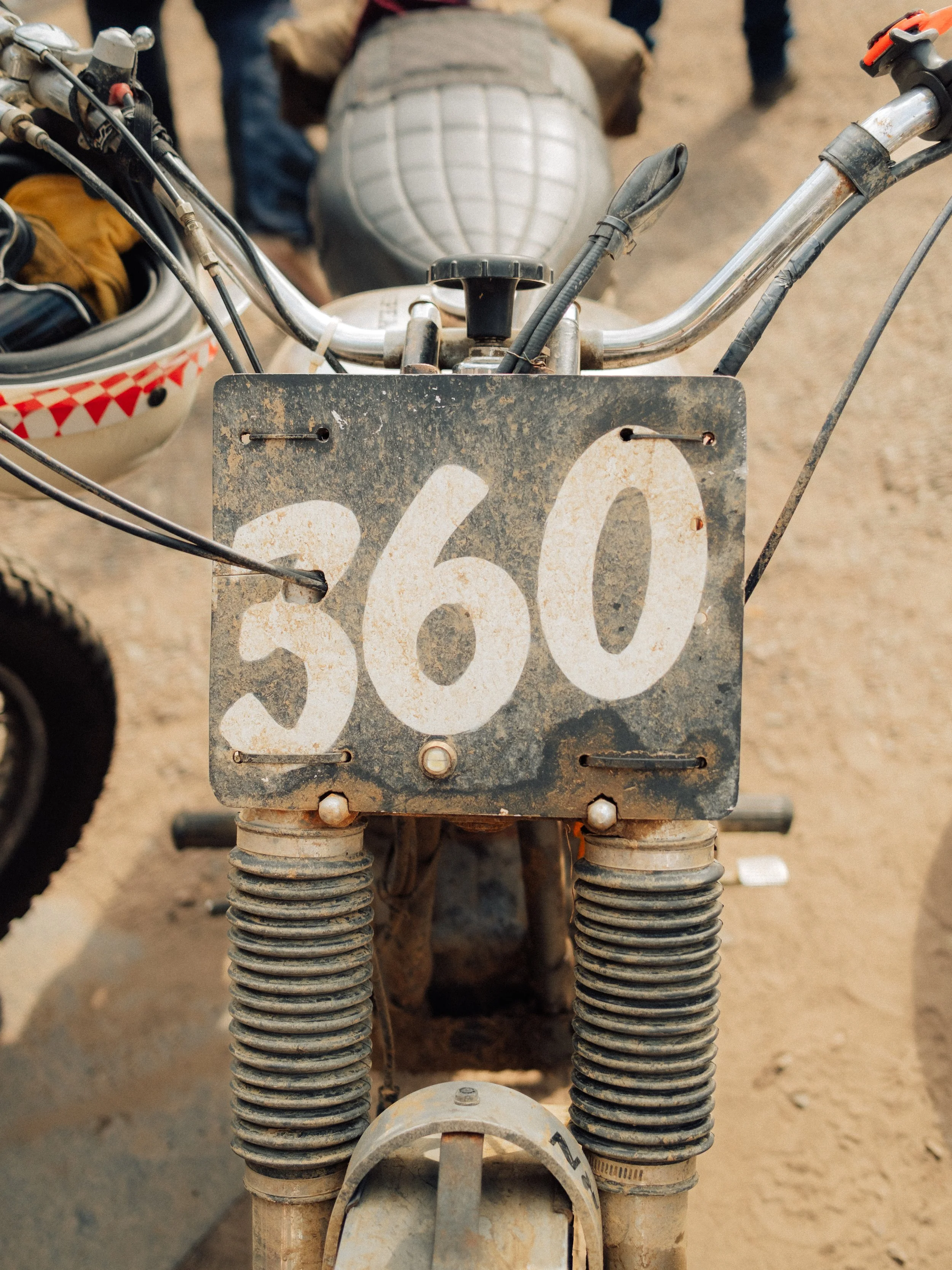 Close-up of a vintage motorcycle handlebar, cables, speedometer, and weathered number plate