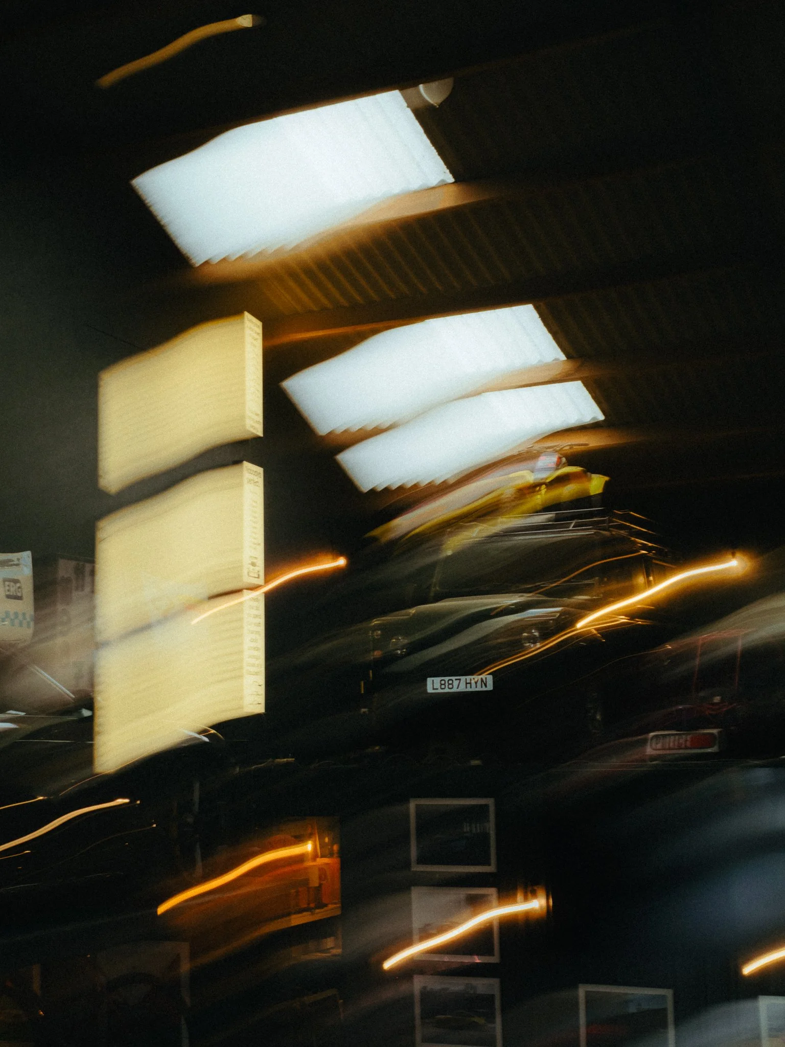 Motion-blurred nighttime street scene with illuminated storefront signs, a black car, and glowing light trails.