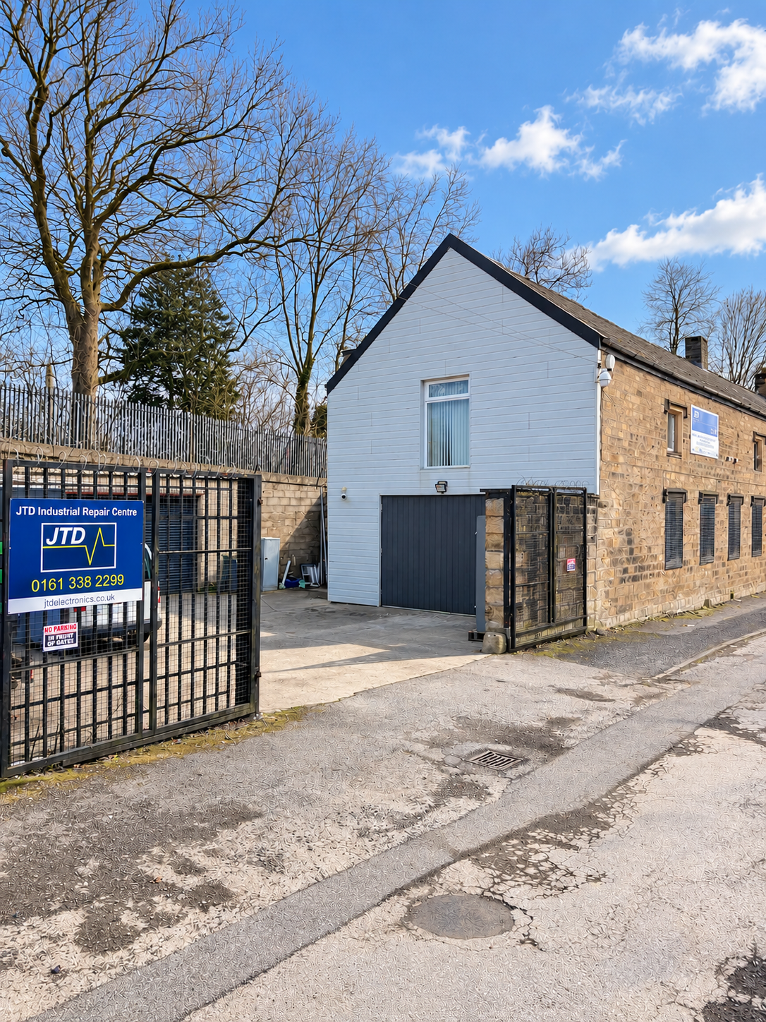 Exterior of JTD Industrial Repair Centre with gated entrance, stone workshop building, and roadside sign.
