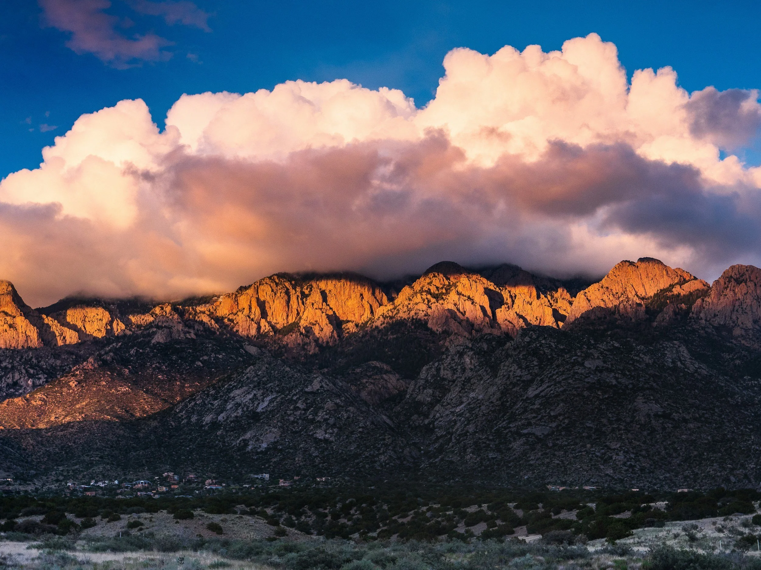 Sunlit rugged mountain range beneath dramatic pink and white clouds