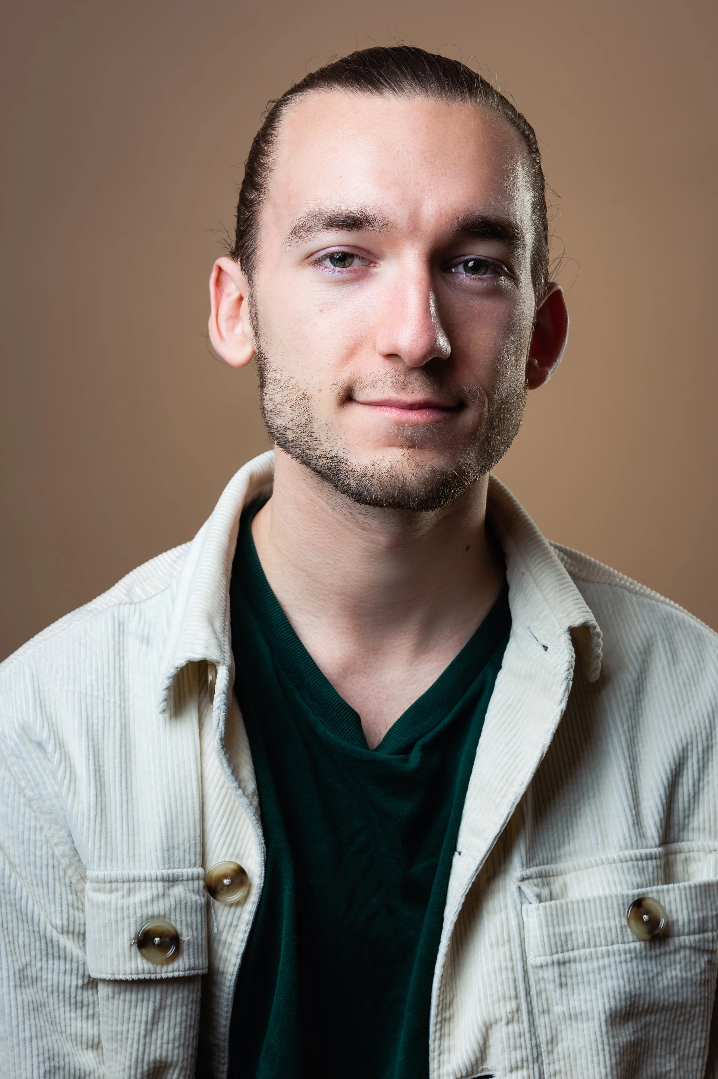 Close-up portrait of a bearded man with slicked-back hair wearing a white corduroy jacket and dark green shirt