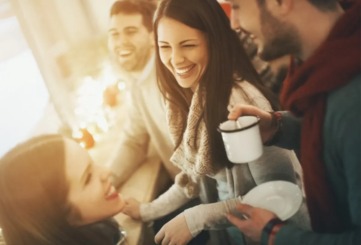 Friends laughing together indoors while holding mugs and plates