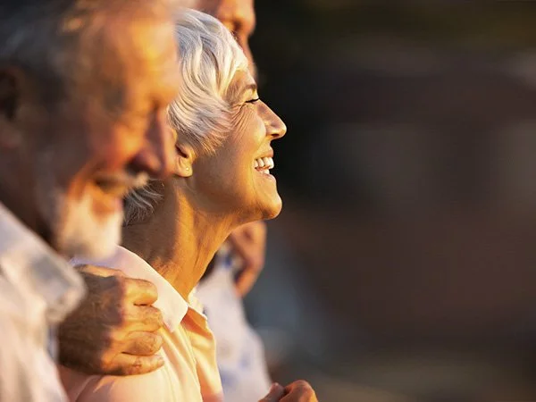 Smiling older woman with short white hair surrounded by friends in warm sunlight
